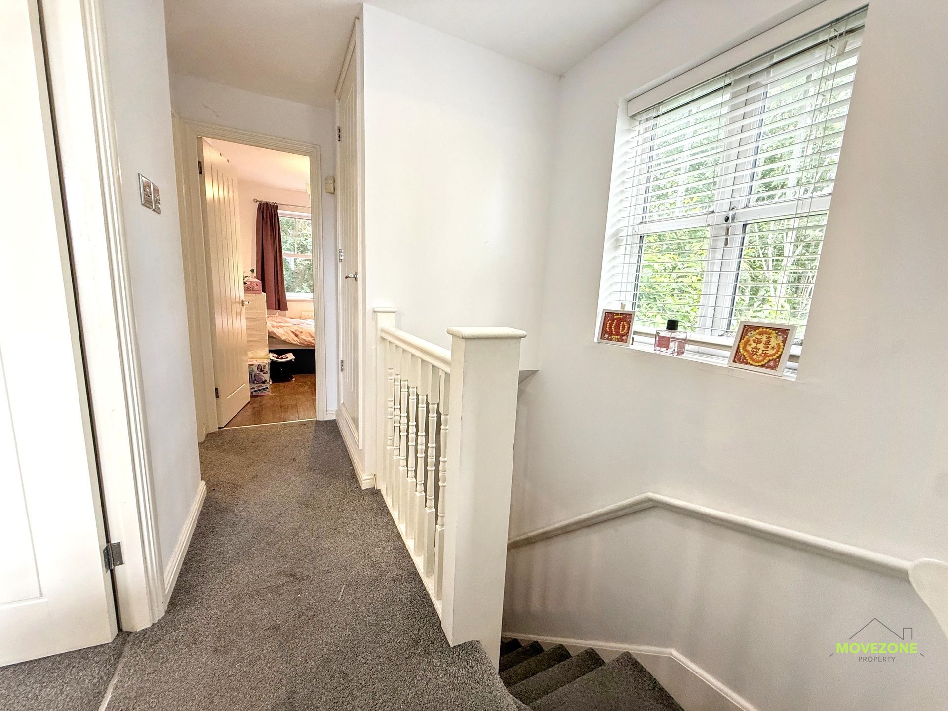 Bright hallway with gray carpet, white walls, stair railing, and a window above the stairs