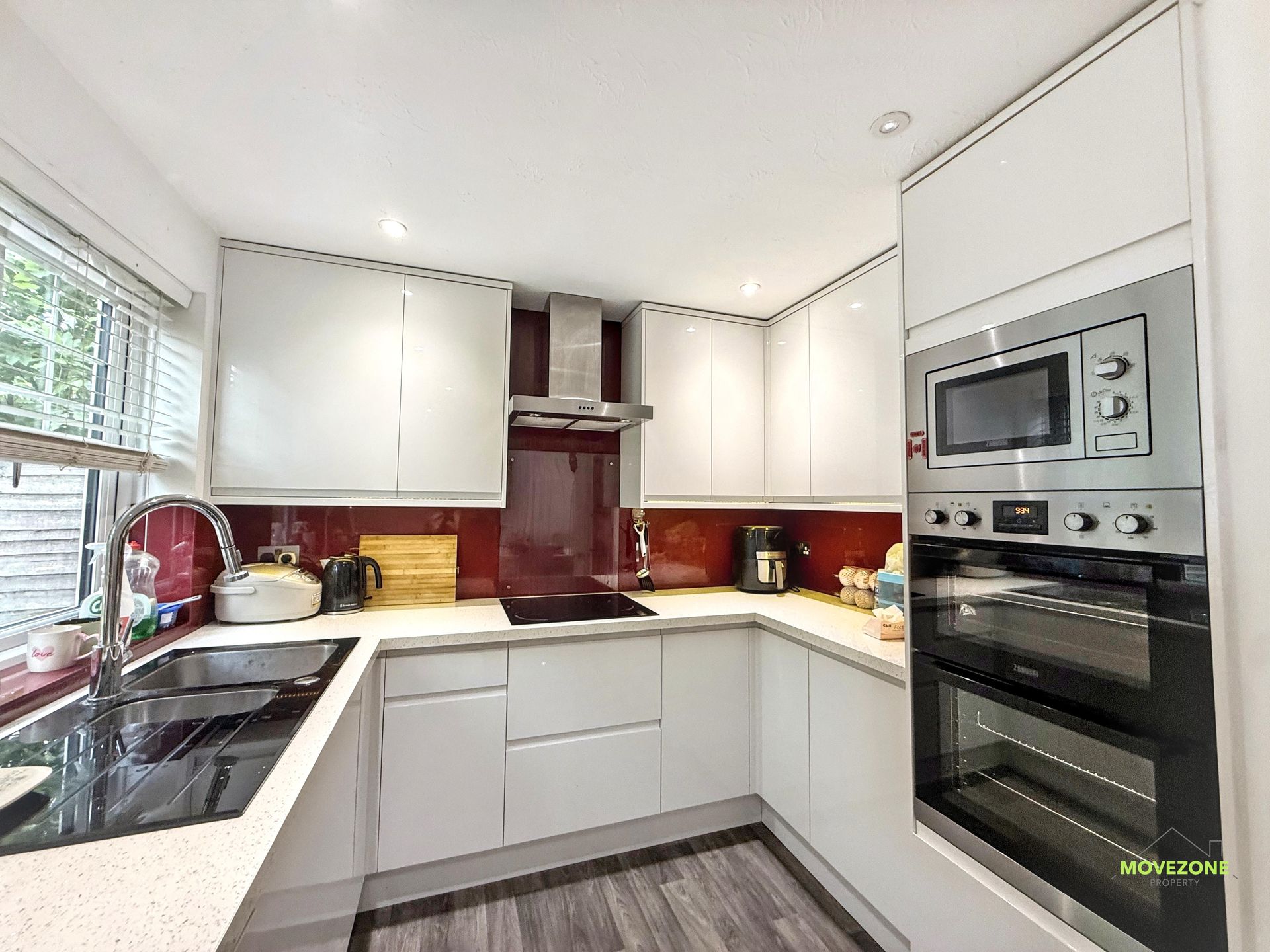 Bright modern kitchen with white cabinets, red backsplash, black countertops, and built-in oven and microwave.