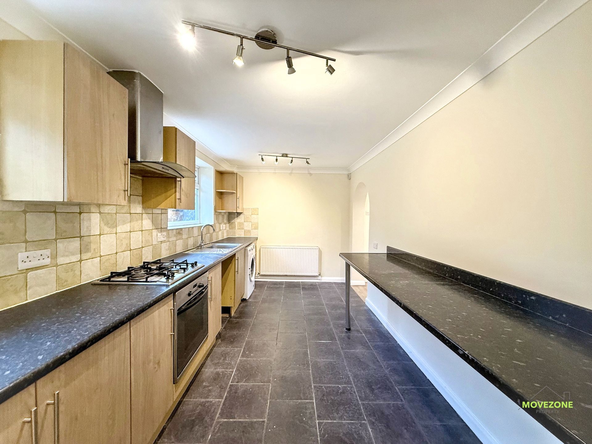 Modern galley kitchen with light wood cabinets, black countertops, and dark tiled floor