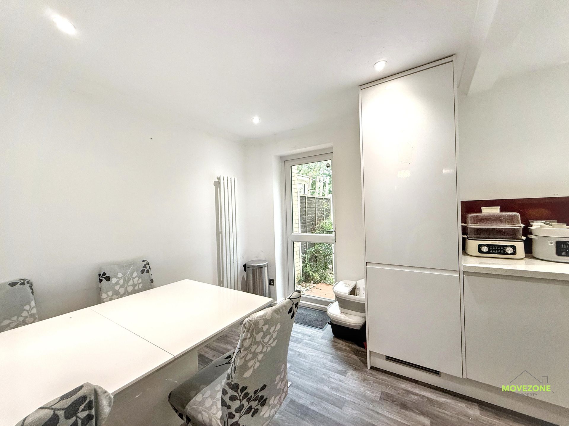 Bright dining room with white table, patterned chairs, tall cabinet, and open door to greenery