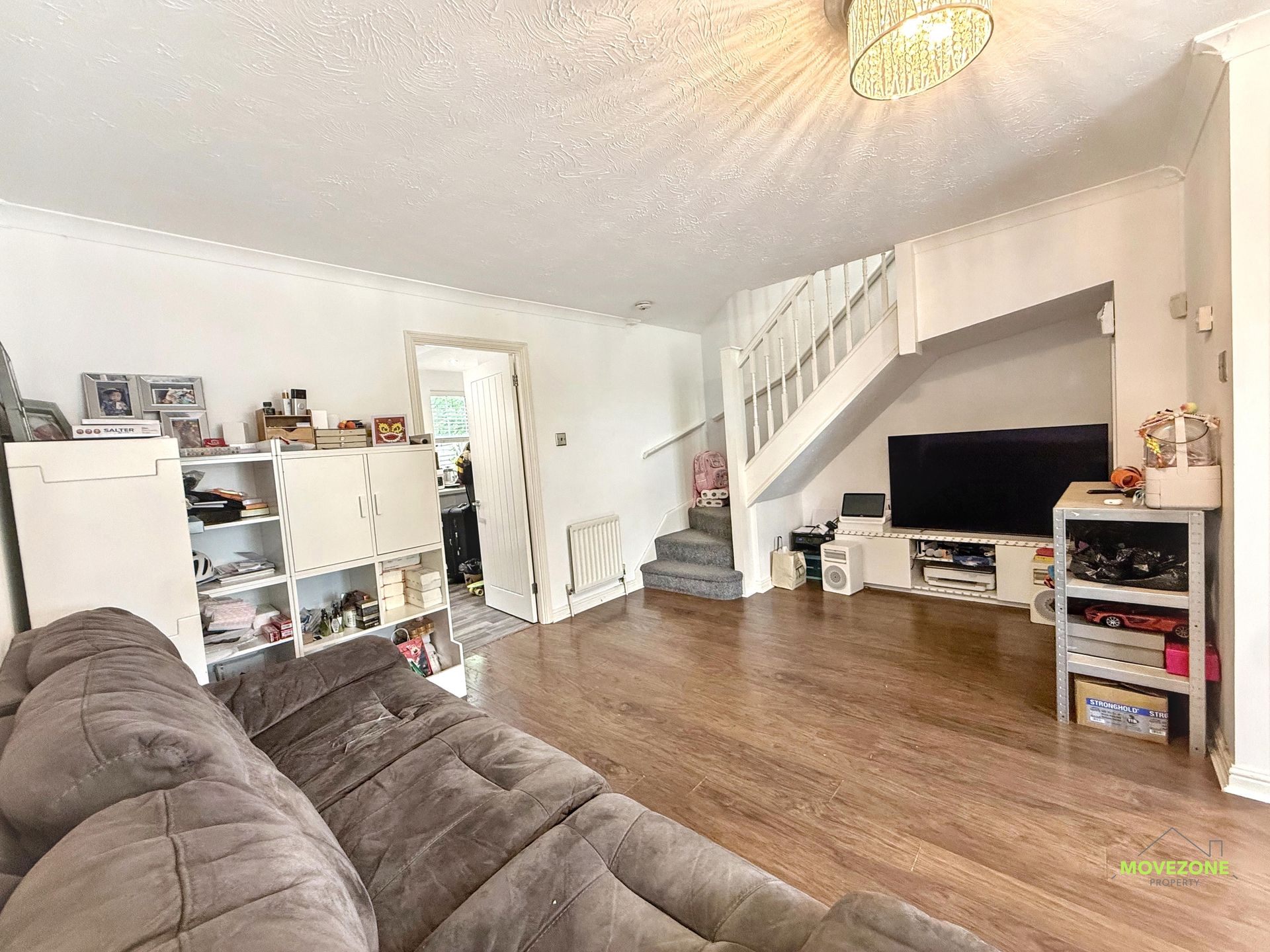 Bright living room with brown sofa, TV, white shelving, and staircase in the background