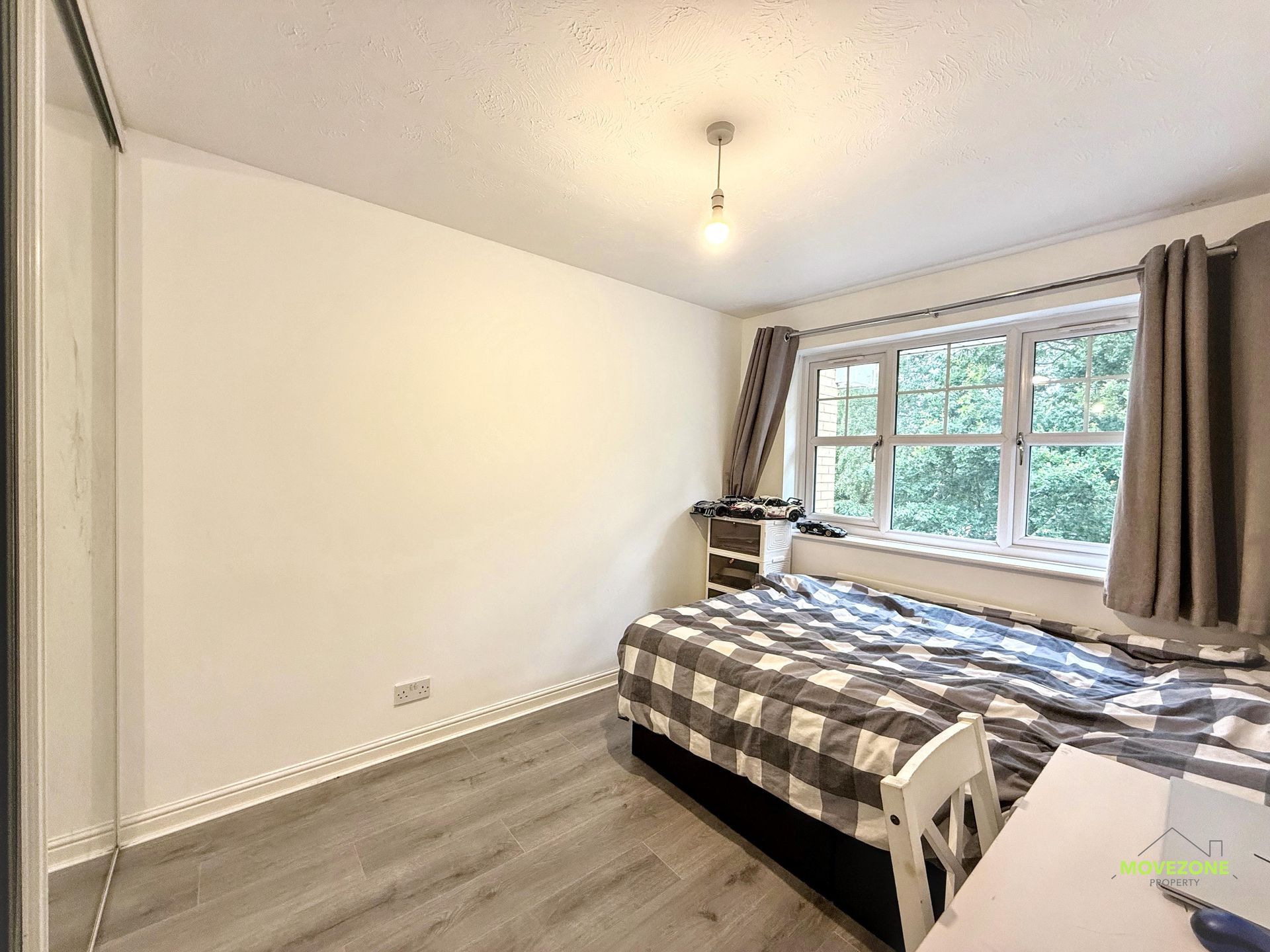 Bright bedroom with a bed by a large window, gray curtains, and light wood flooring