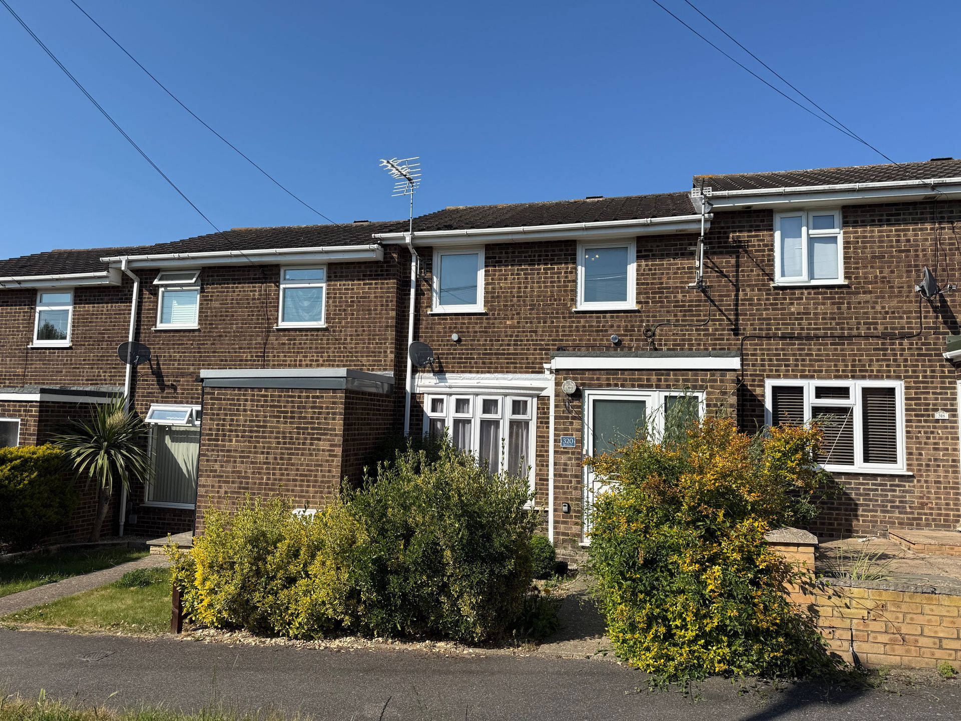 Row of brick terraced houses with small front gardens under a clear blue sky