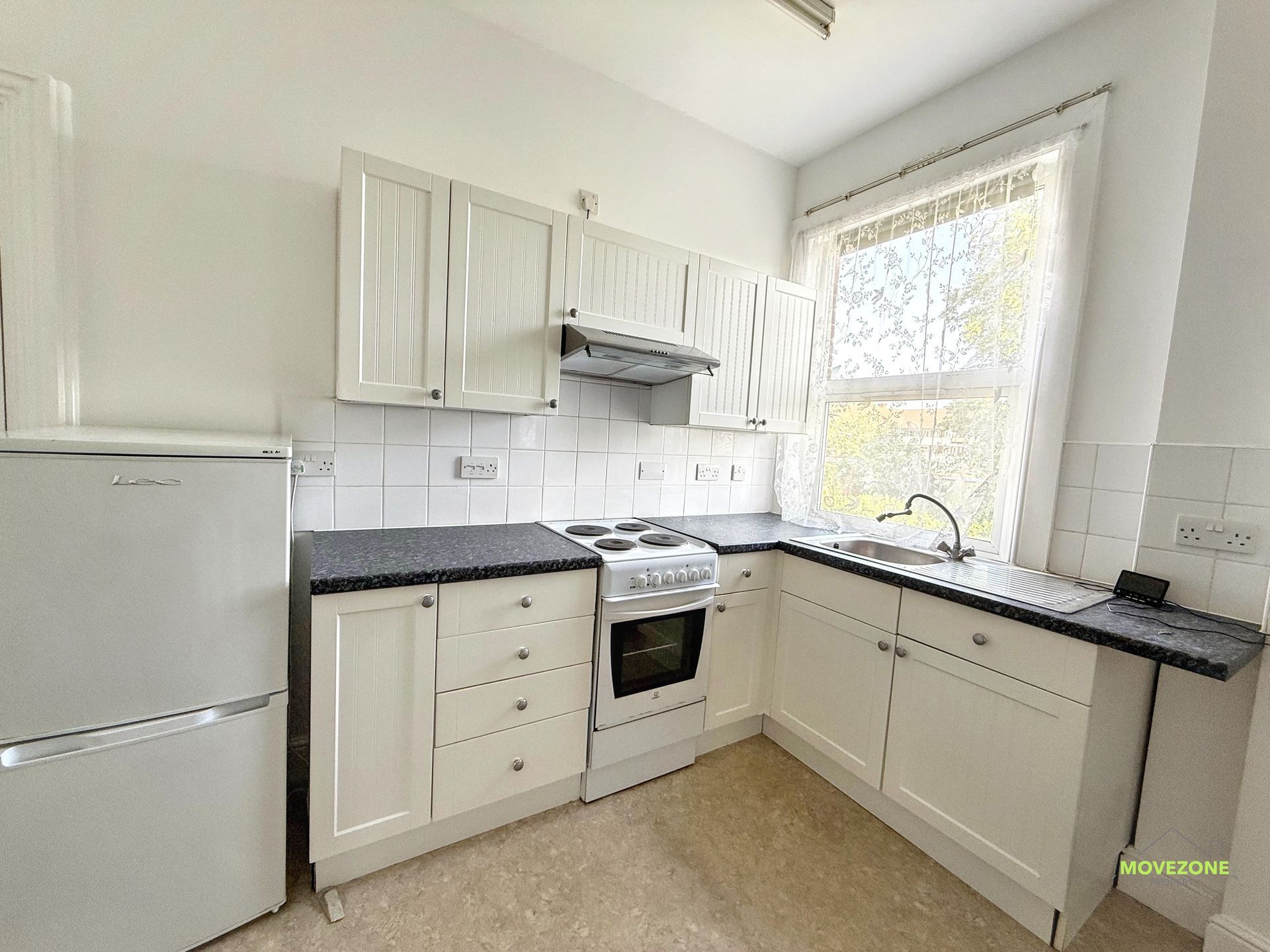 Bright white kitchen with black countertops, white cabinets, stove, fridge, and large window.