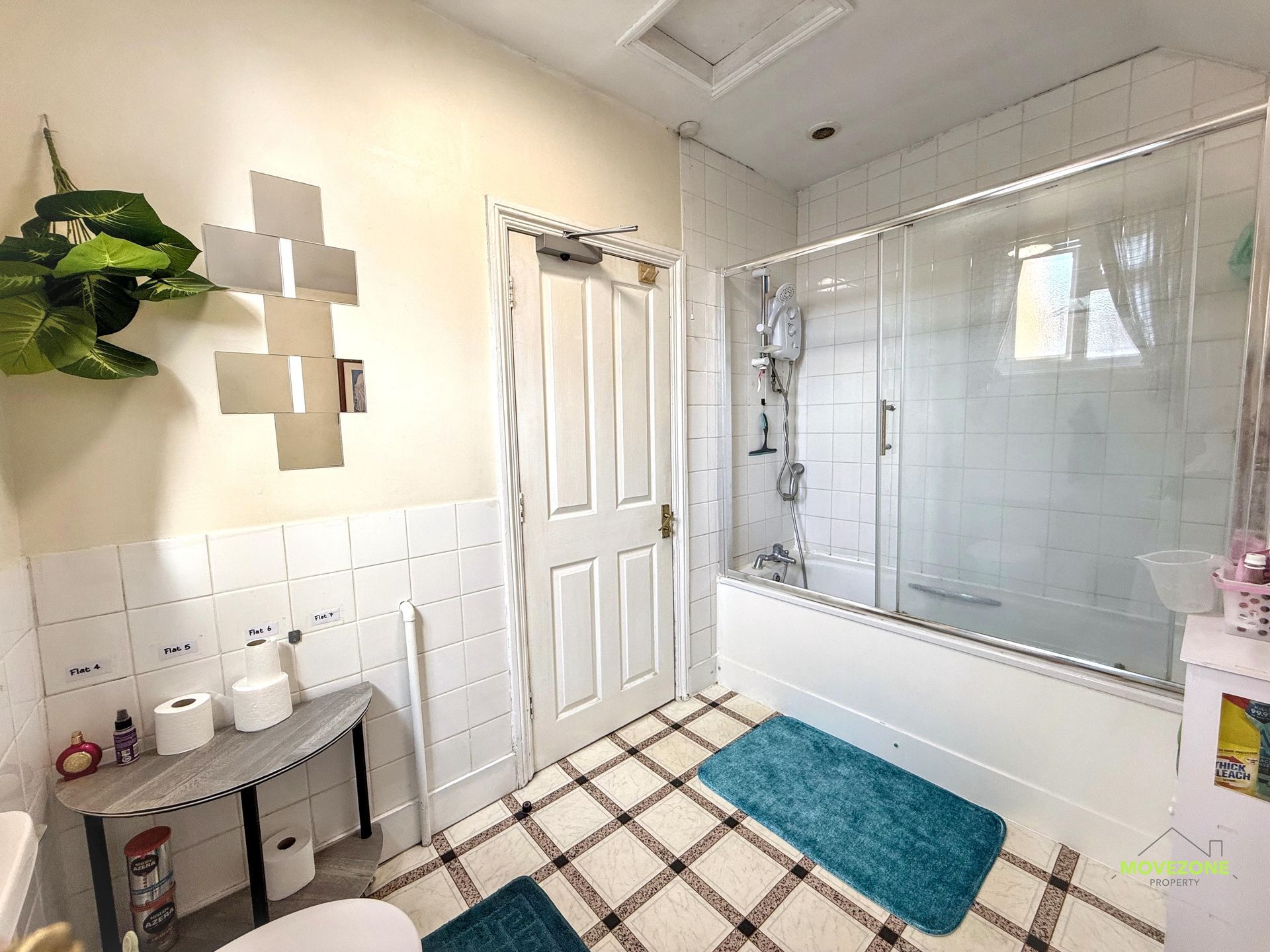 Bright bathroom with white tile, glass shower, teal bath mat, and small sink table.