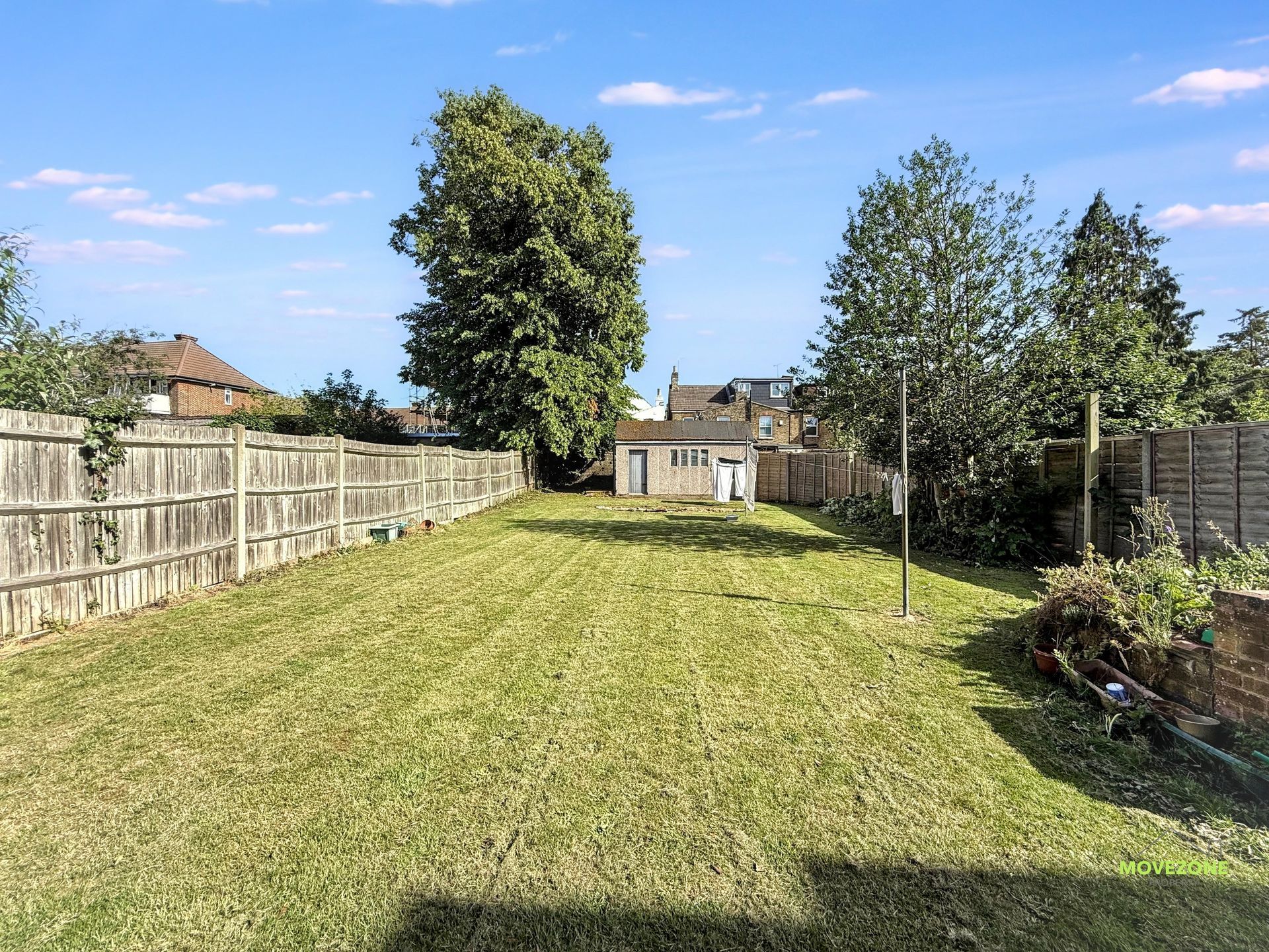 Large mowed backyard with wooden fences, trees, and a small shed under a blue sky