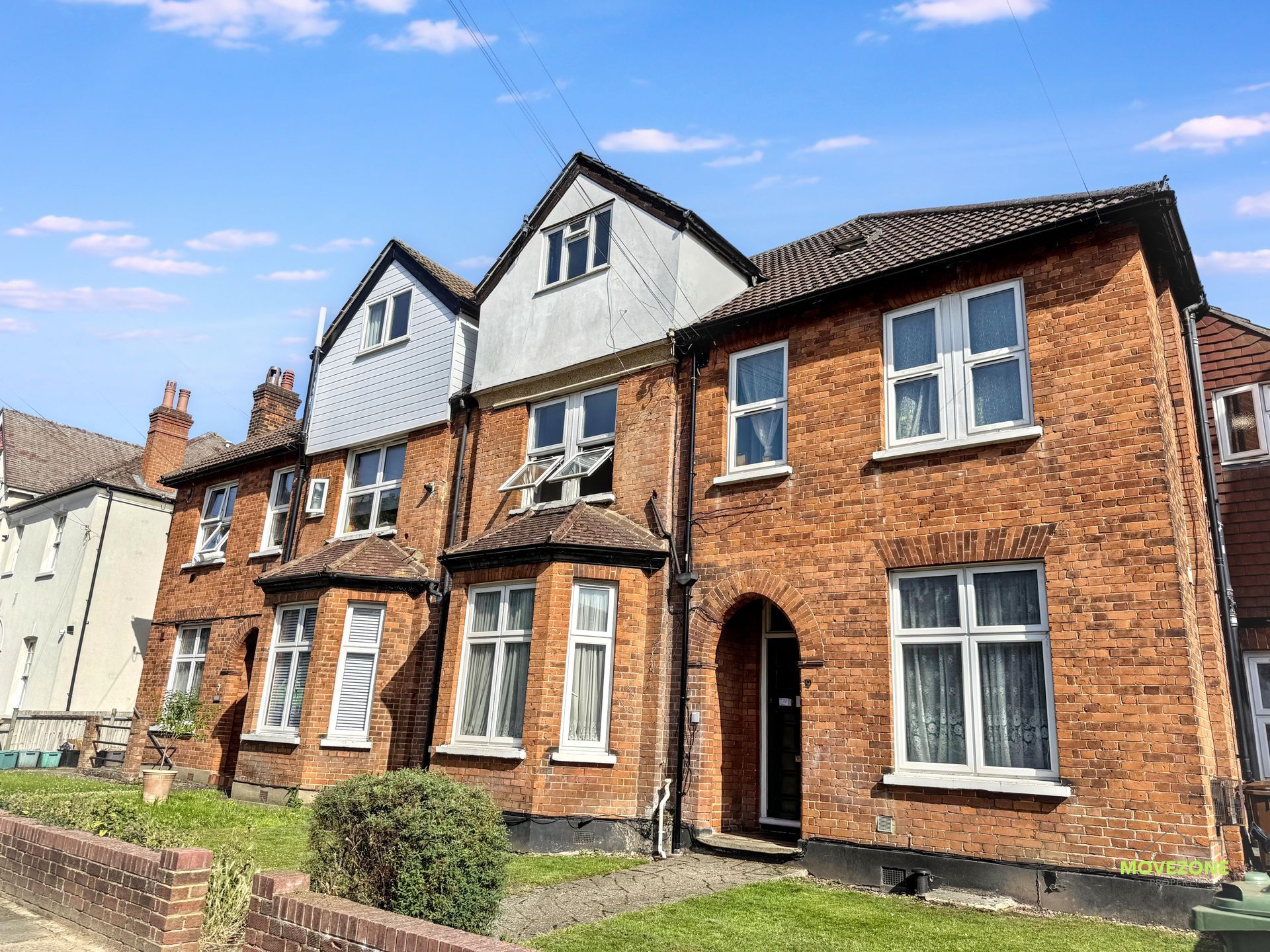 Row of red-brick terraced houses with white-trimmed windows under a blue sky