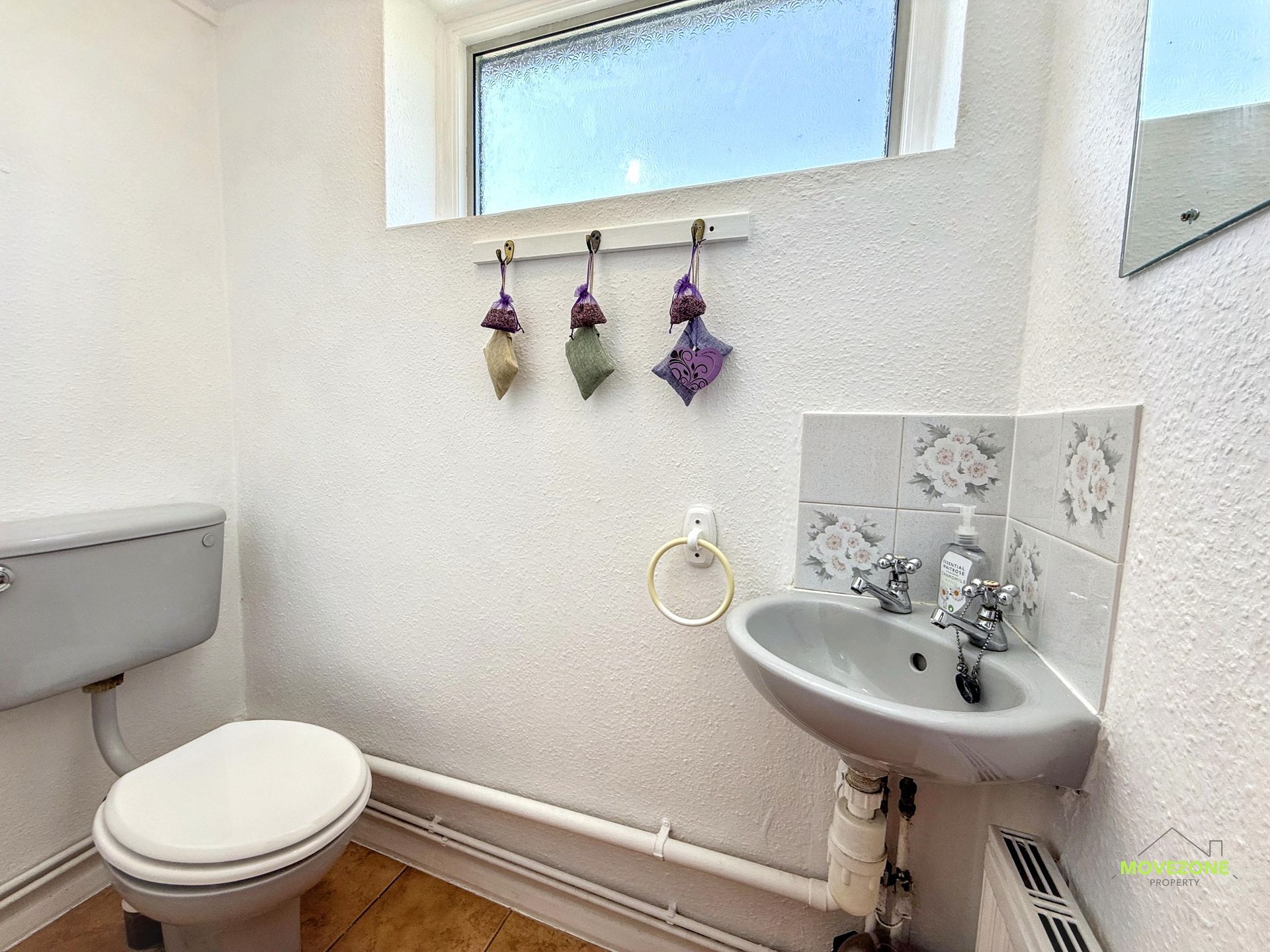 Small white bathroom with toilet, sink, frosted window, and purple hanging decor