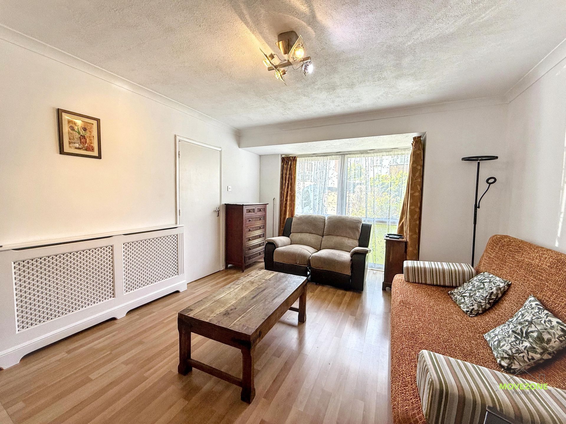 Bright living room with sofa, coffee table, striped armchair, white walls, wood floor, and large window