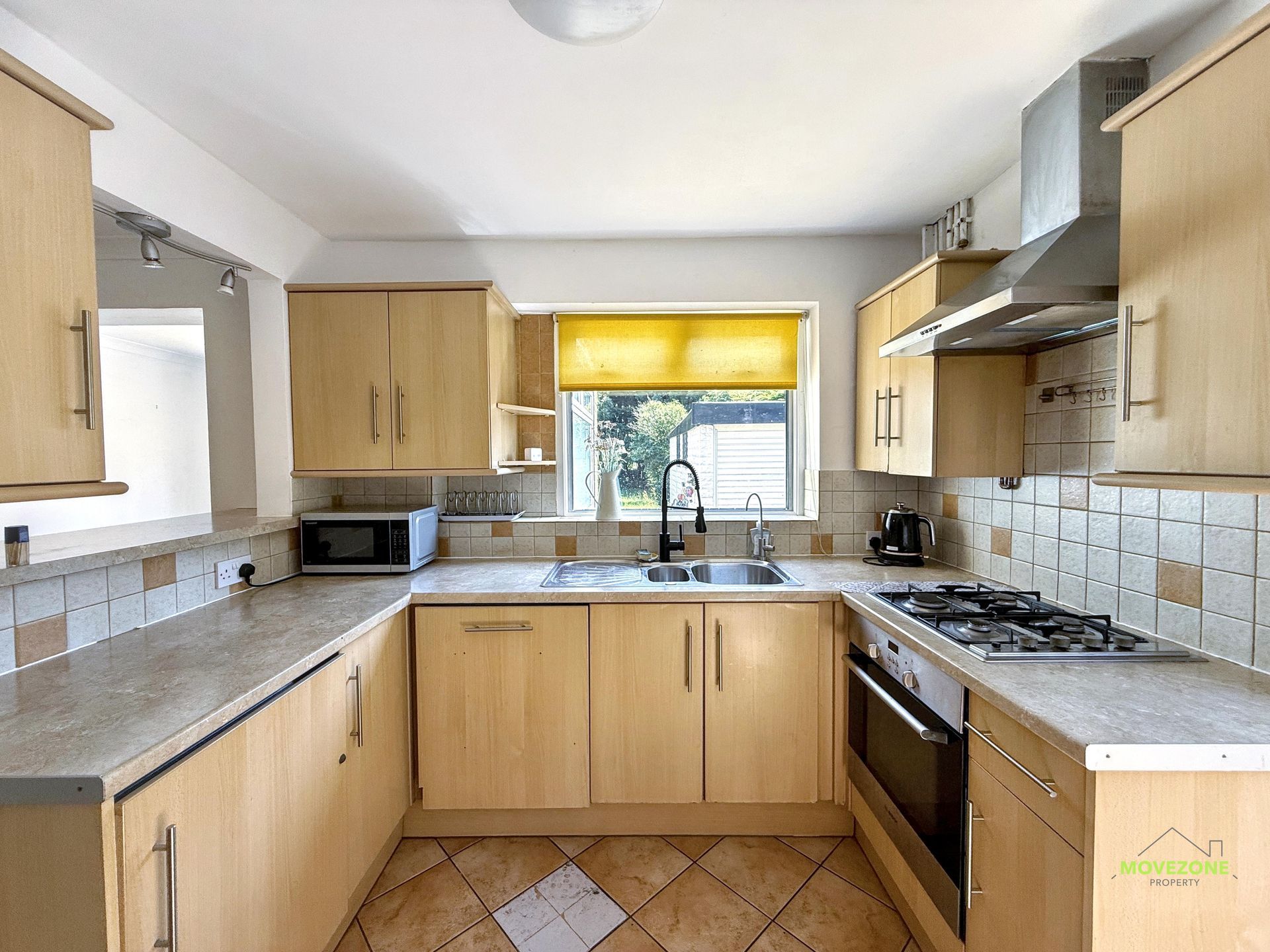 Bright modern kitchen with wood cabinets, granite counters, and a gas stove by a window.