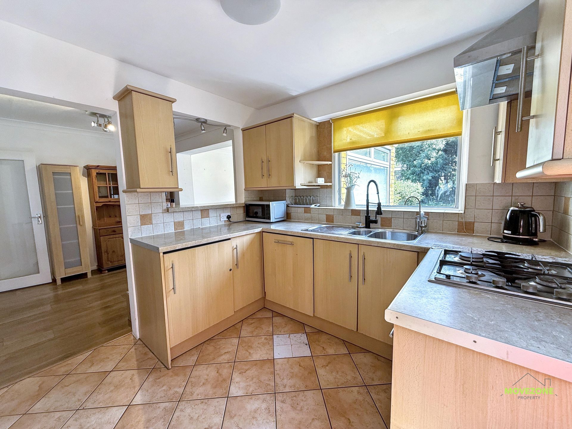 Bright modern kitchen with light wood cabinets, tiled floor, and a large window over the sink.
