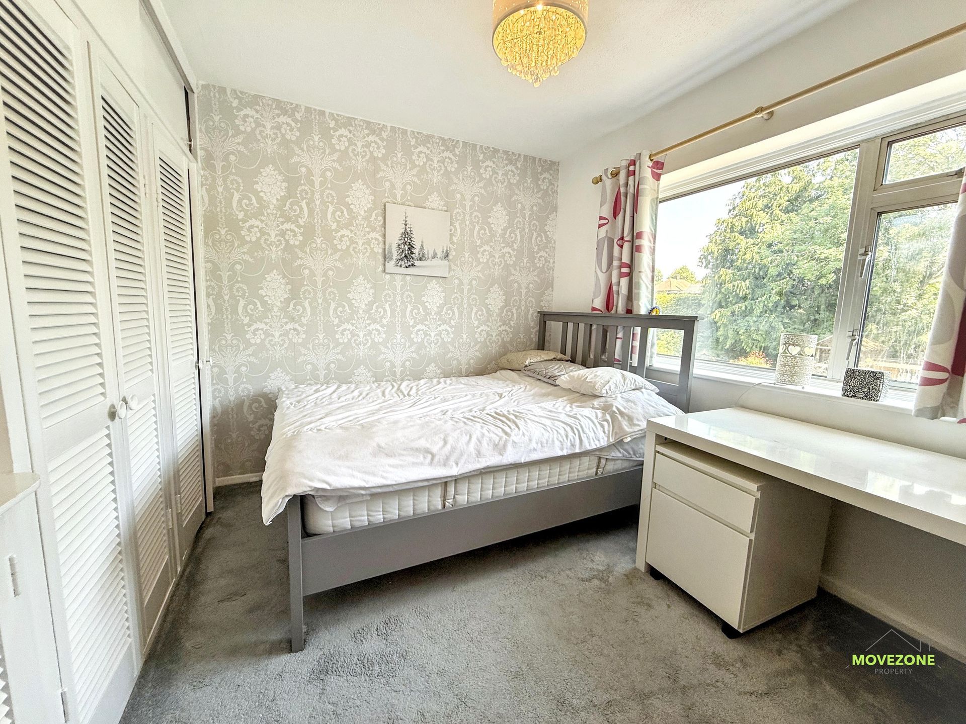 Bright bedroom with white bed, large window, desk, and gray carpet.