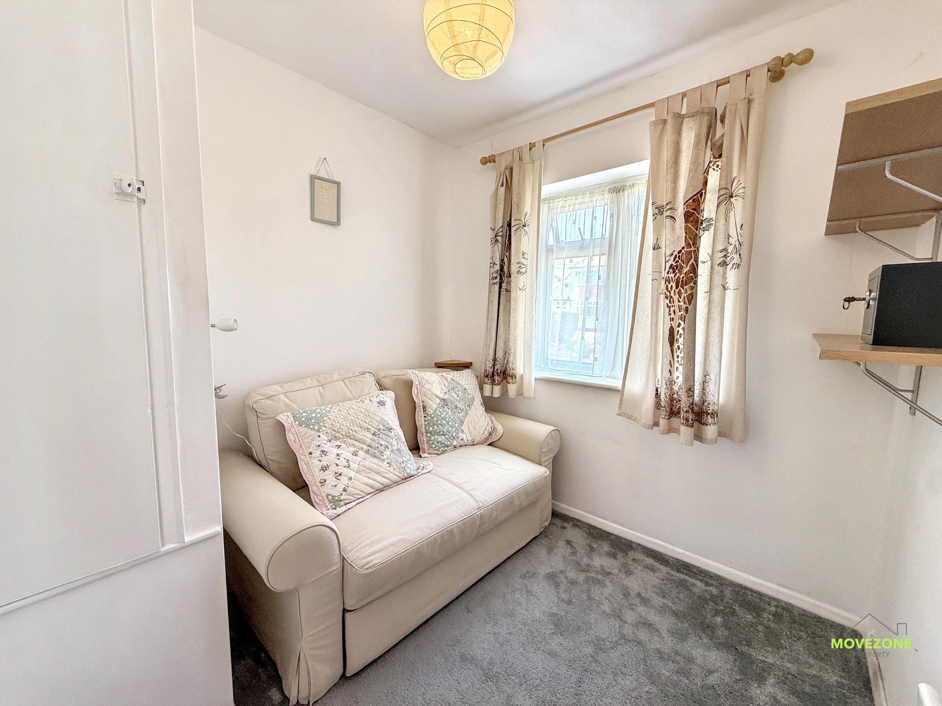 Small white room with a beige loveseat, window with curtains, gray carpet, and wall shelves.
