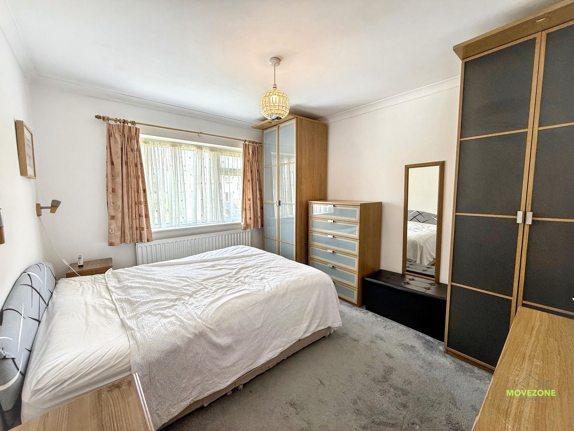 Bright bedroom with a bed, window, dresser, mirror, and black wardrobe on a gray carpet