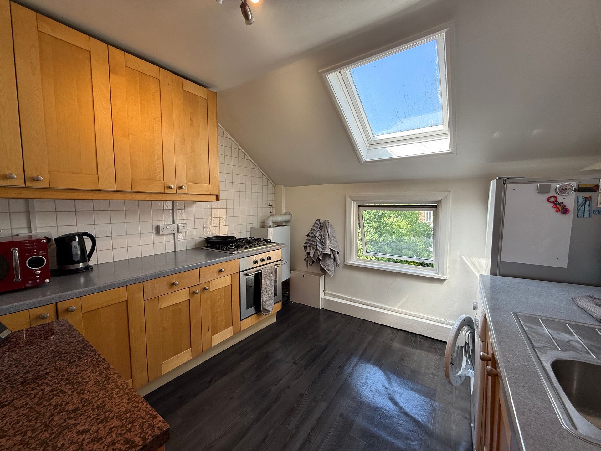 Bright kitchen with wooden cabinets, black floor, skylight, and window over the sink