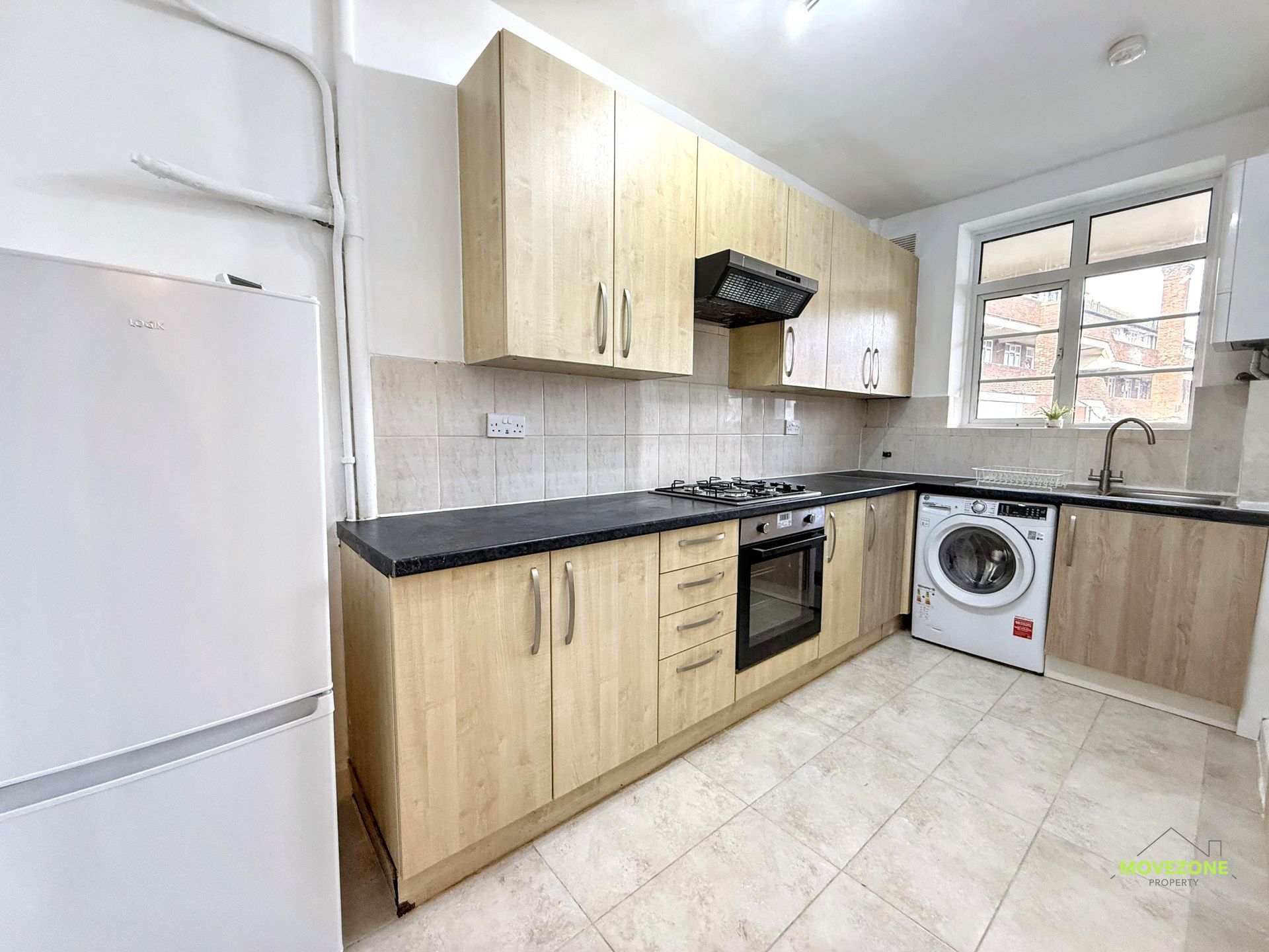 Compact white kitchen with wood cabinets, black countertops, stove, fridge, and washing machine