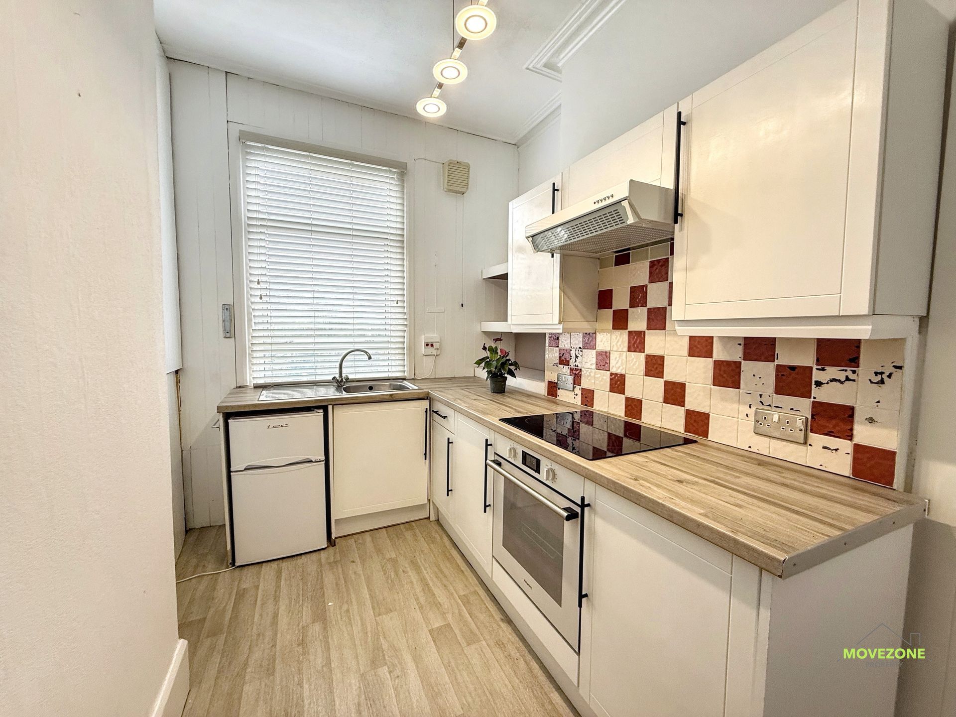Bright narrow galley kitchen with white cabinets, wood countertops, red tile backsplash, and a window over the sink