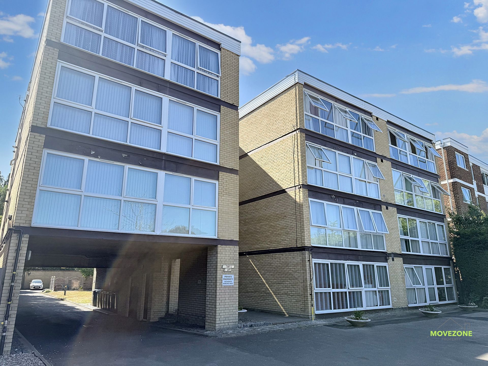 Modern apartment buildings with large windows and an open ground-level passageway under a blue sky