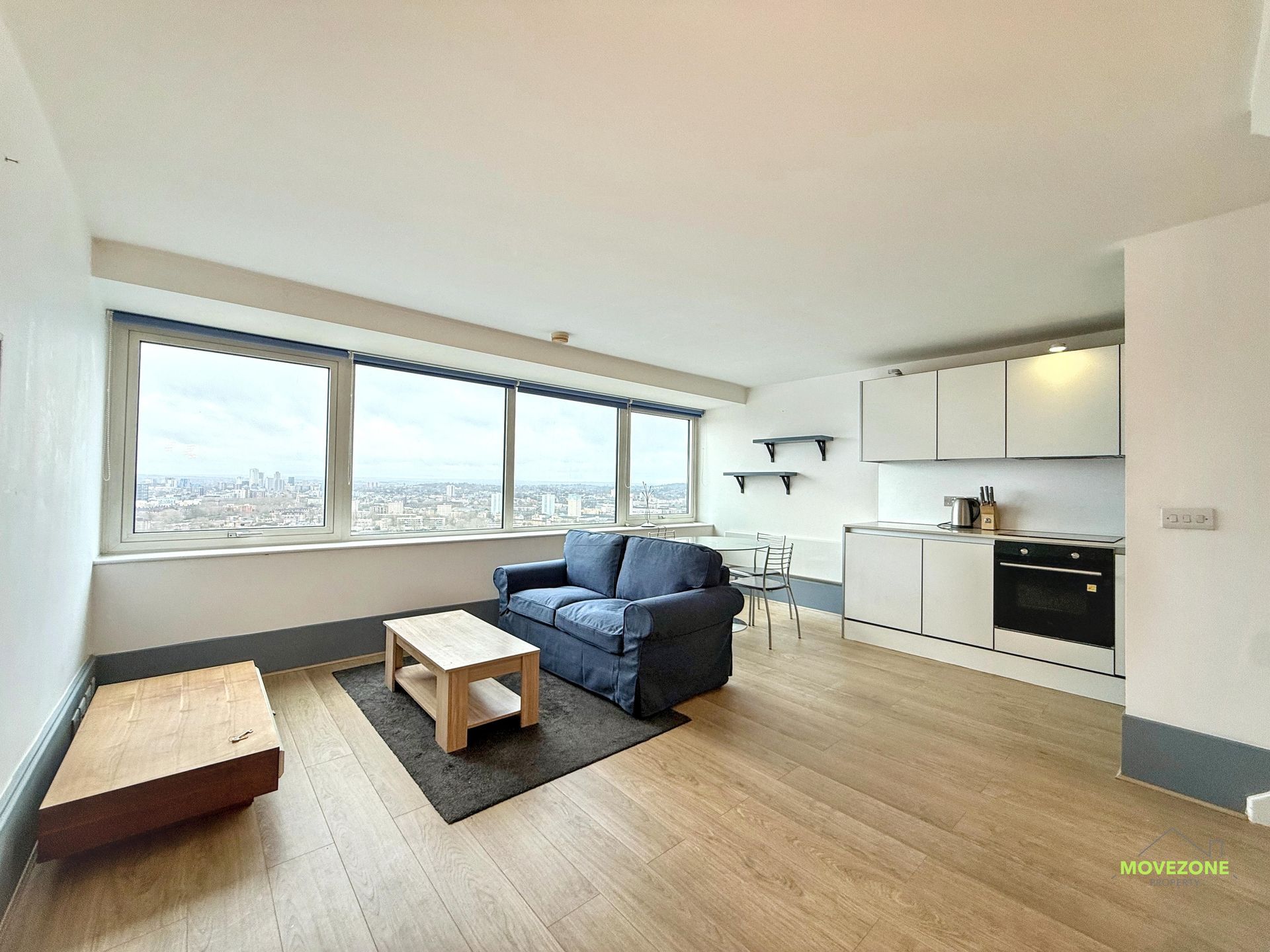 Bright modern living room with sofa, coffee table, low bed, and open kitchen by large windows