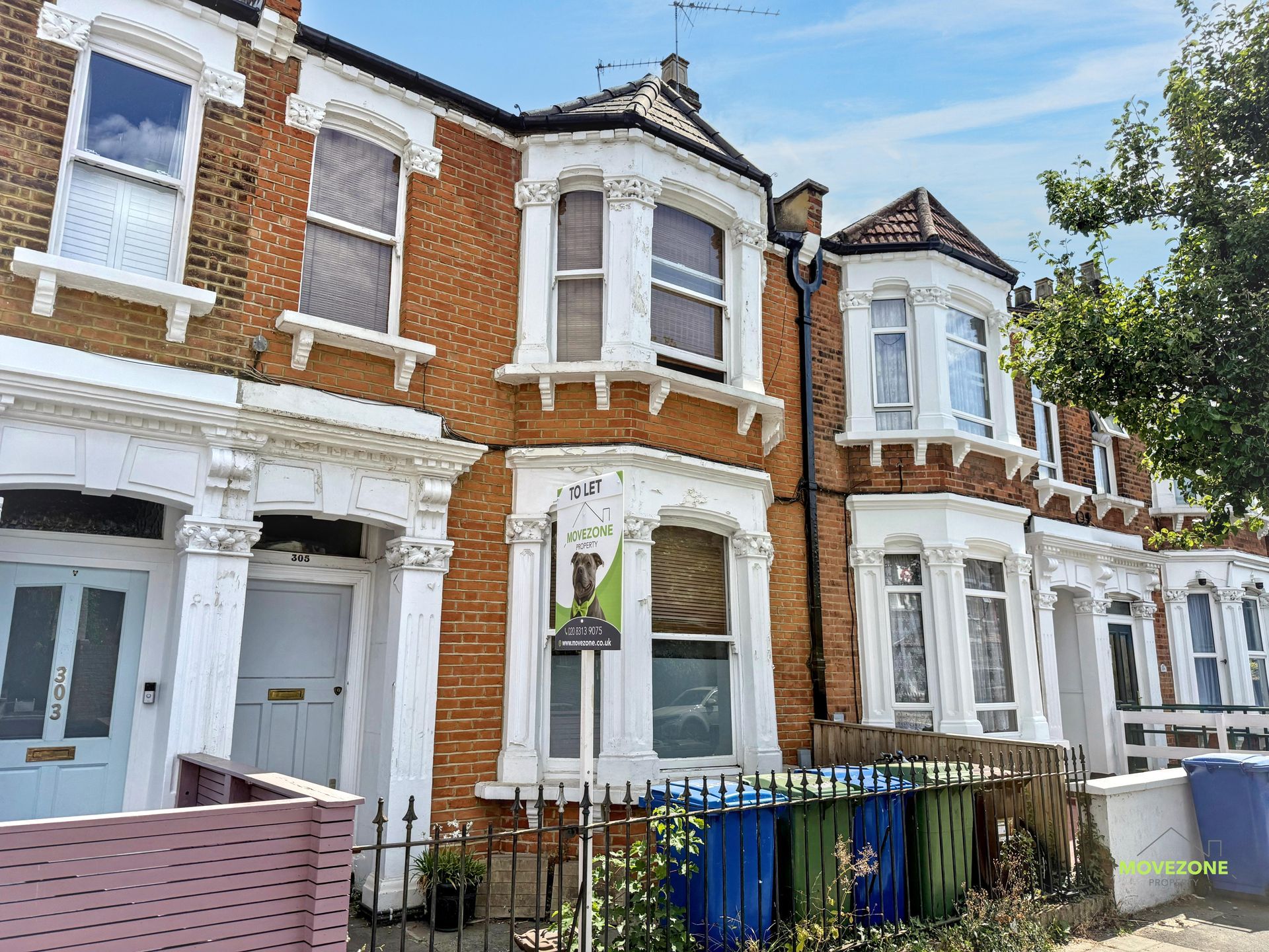 Row of red-brick Victorian houses with white trim and front gardens on a sunny street.