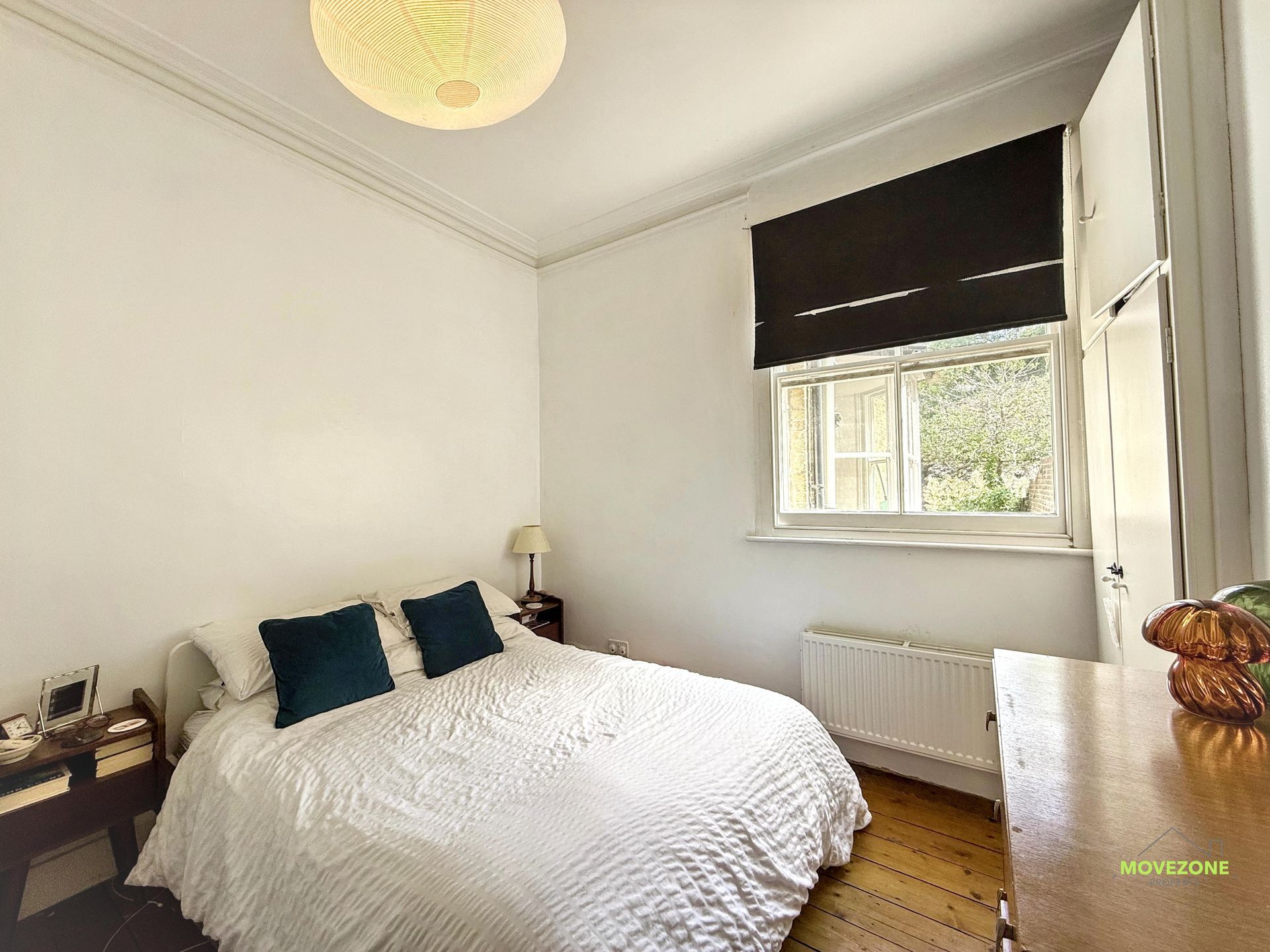 Bright bedroom with white walls, a bed, dark window blind, and wooden floor.