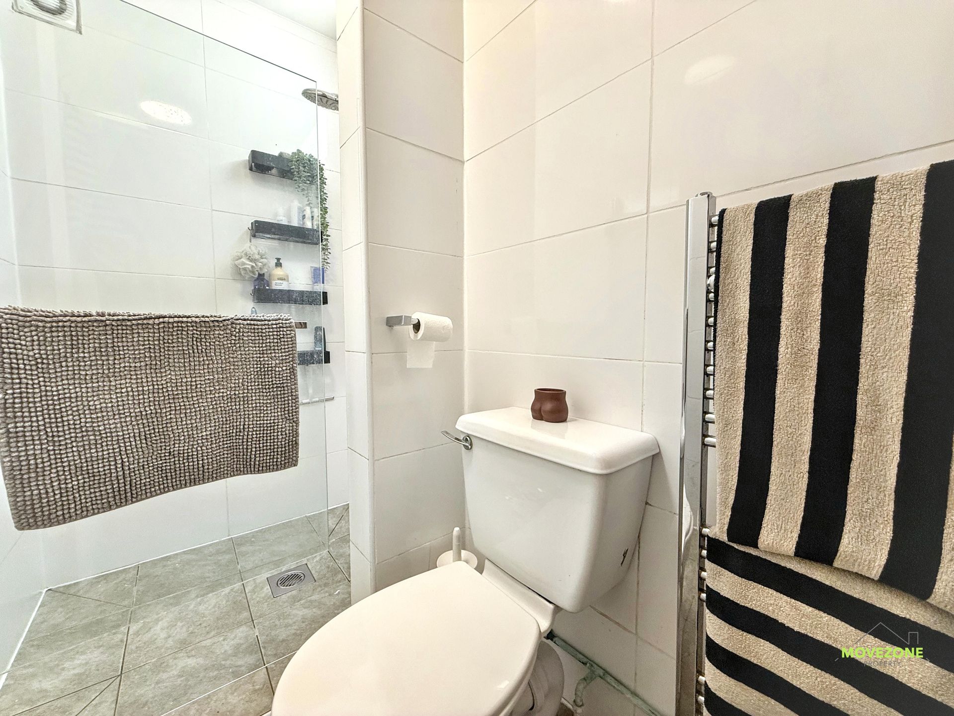 Small bathroom with toilet, white tiled walls, glass shower, and striped towels.