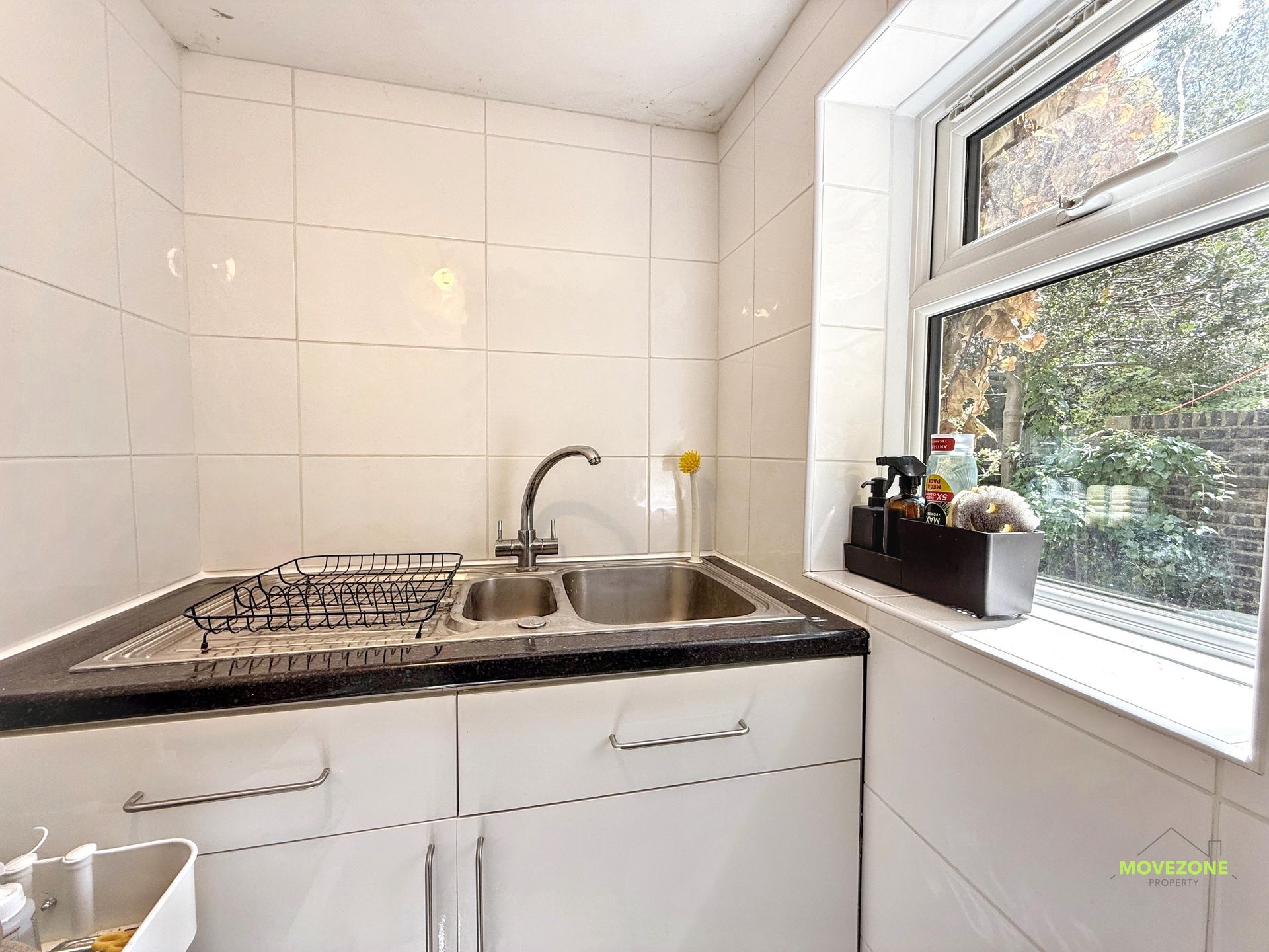 Small white kitchen with sink, dish rack, window, and countertop items