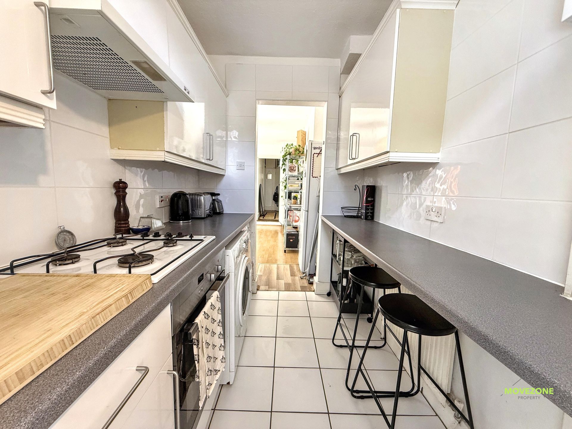 Narrow white galley kitchen with gray countertops, tiled floor, and stools along one side