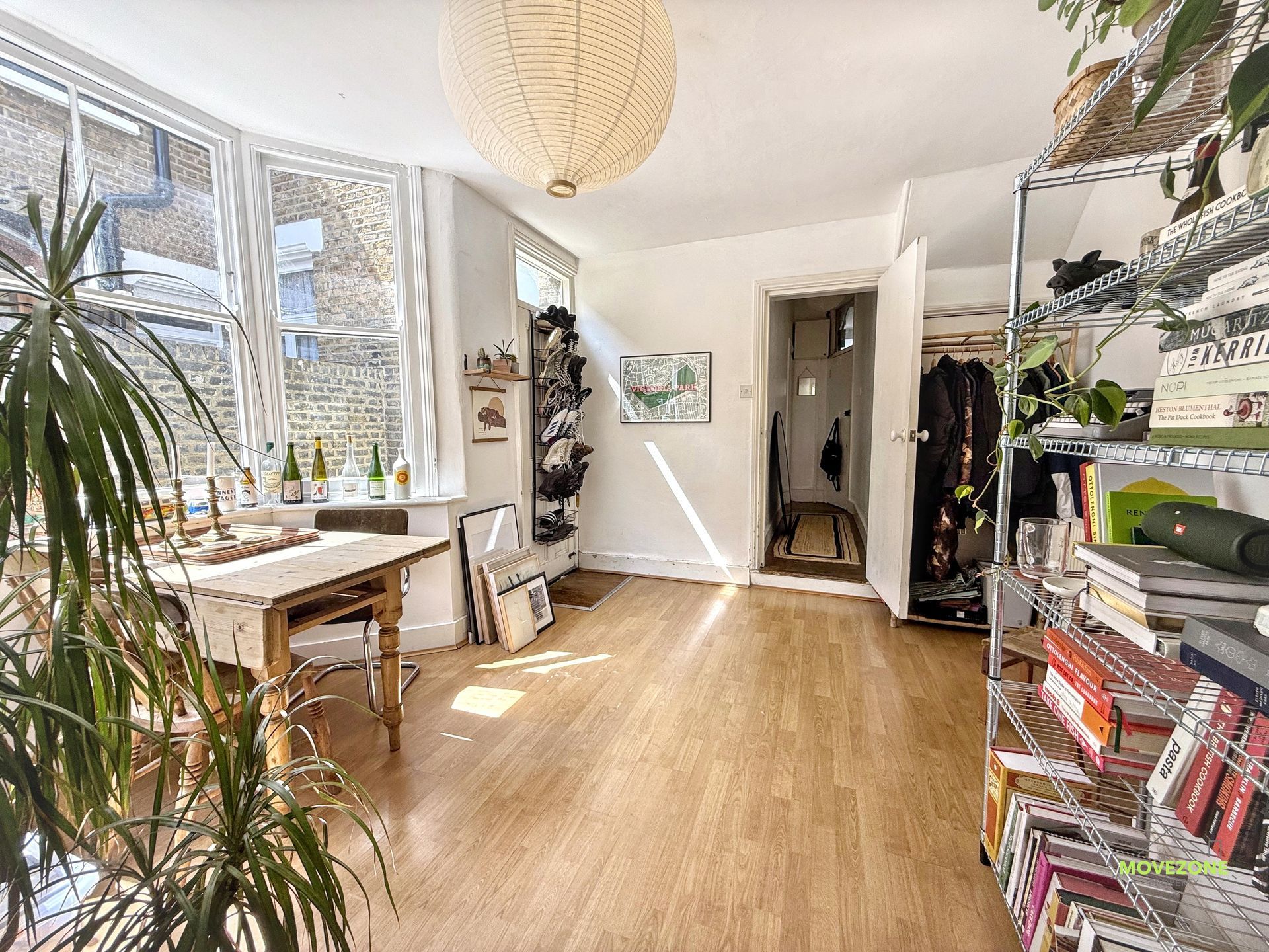 Bright home office with large windows, wooden floor, desk, plants, shelving, and a hanging paper lamp
