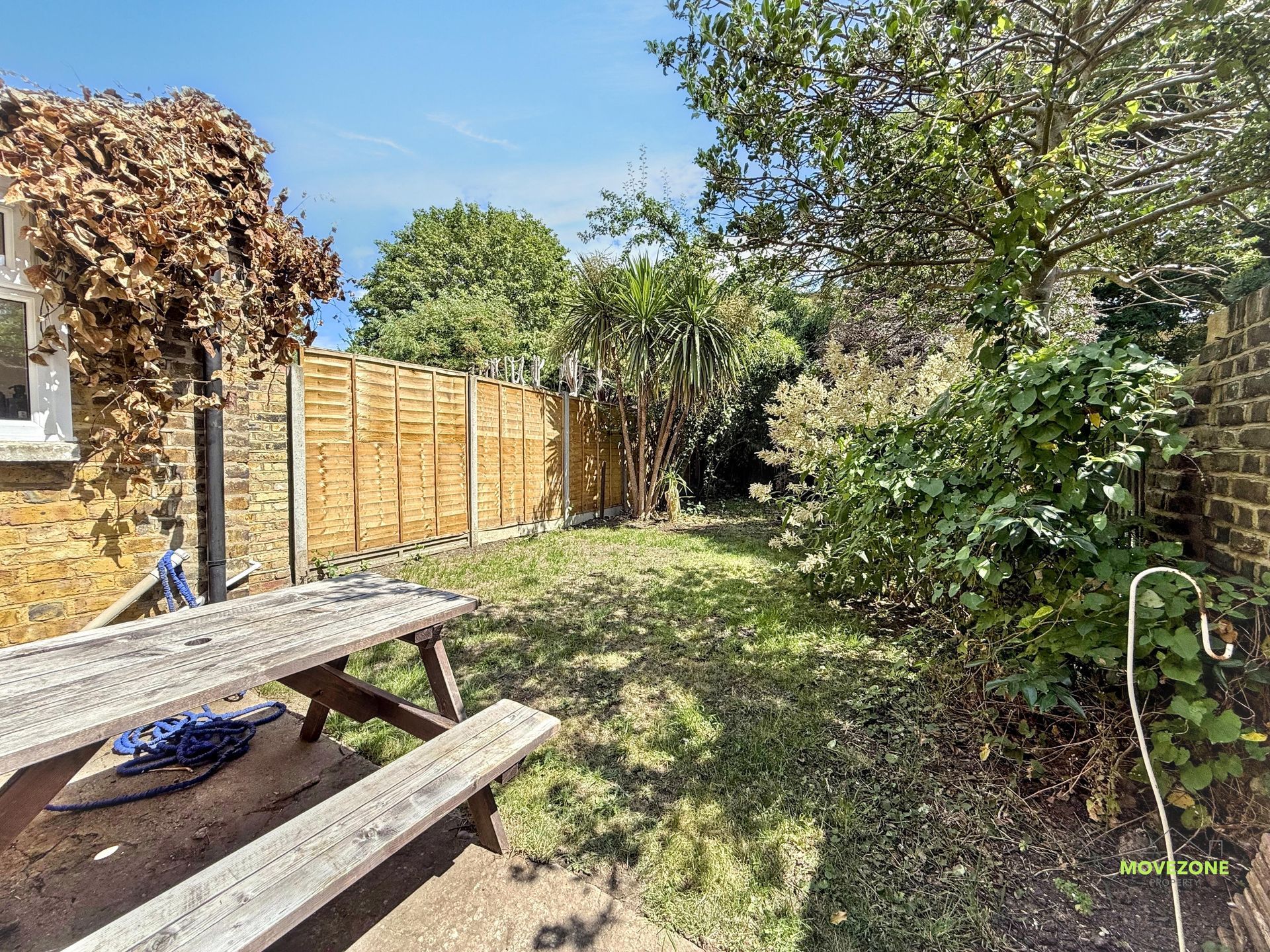 Backyard with picnic table, wooden fence, leafy trees, and a grassy path in sunlight