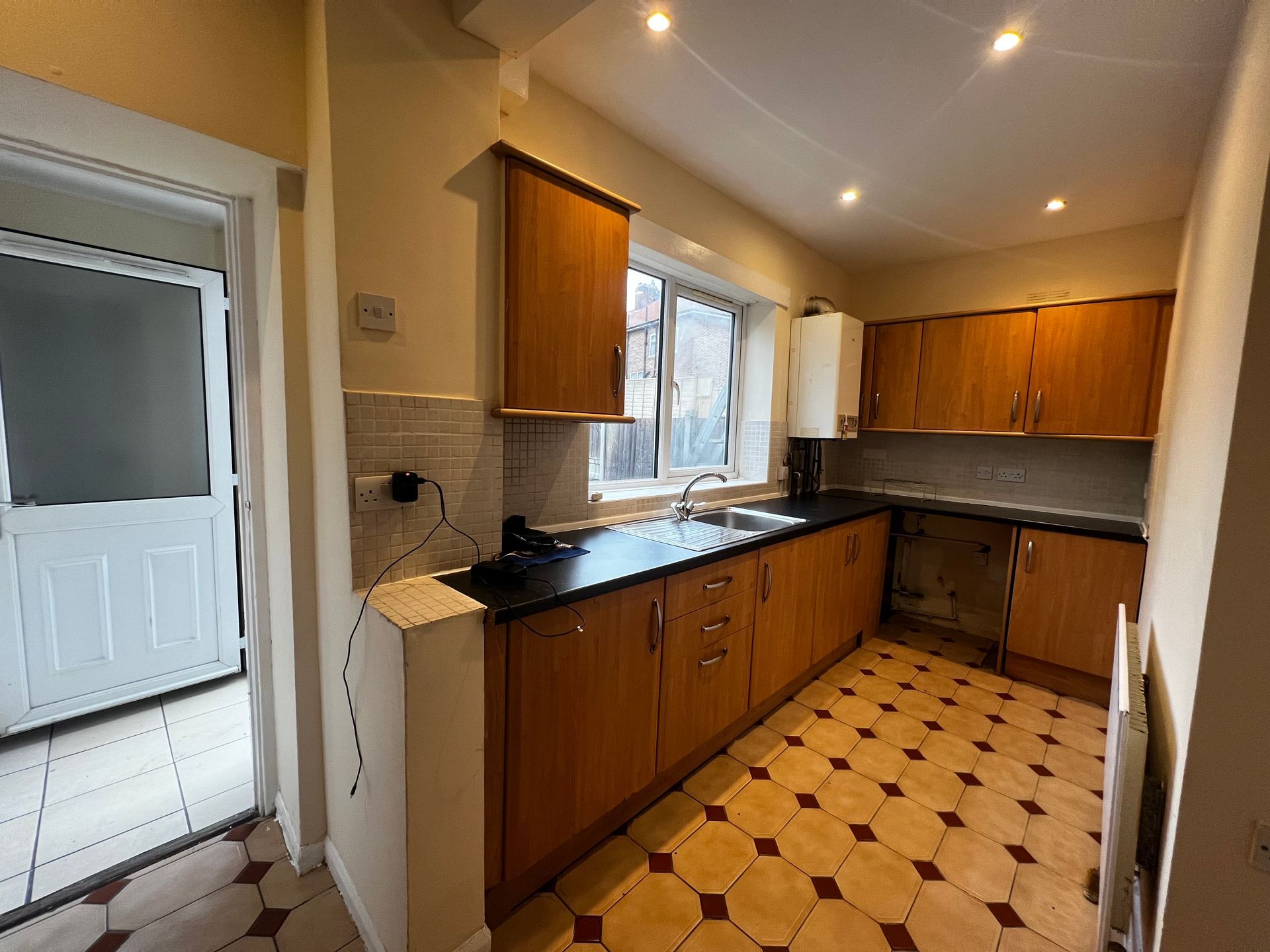 Small kitchen with wood cabinets, black countertops, patterned tile floor, and a window over the sink.