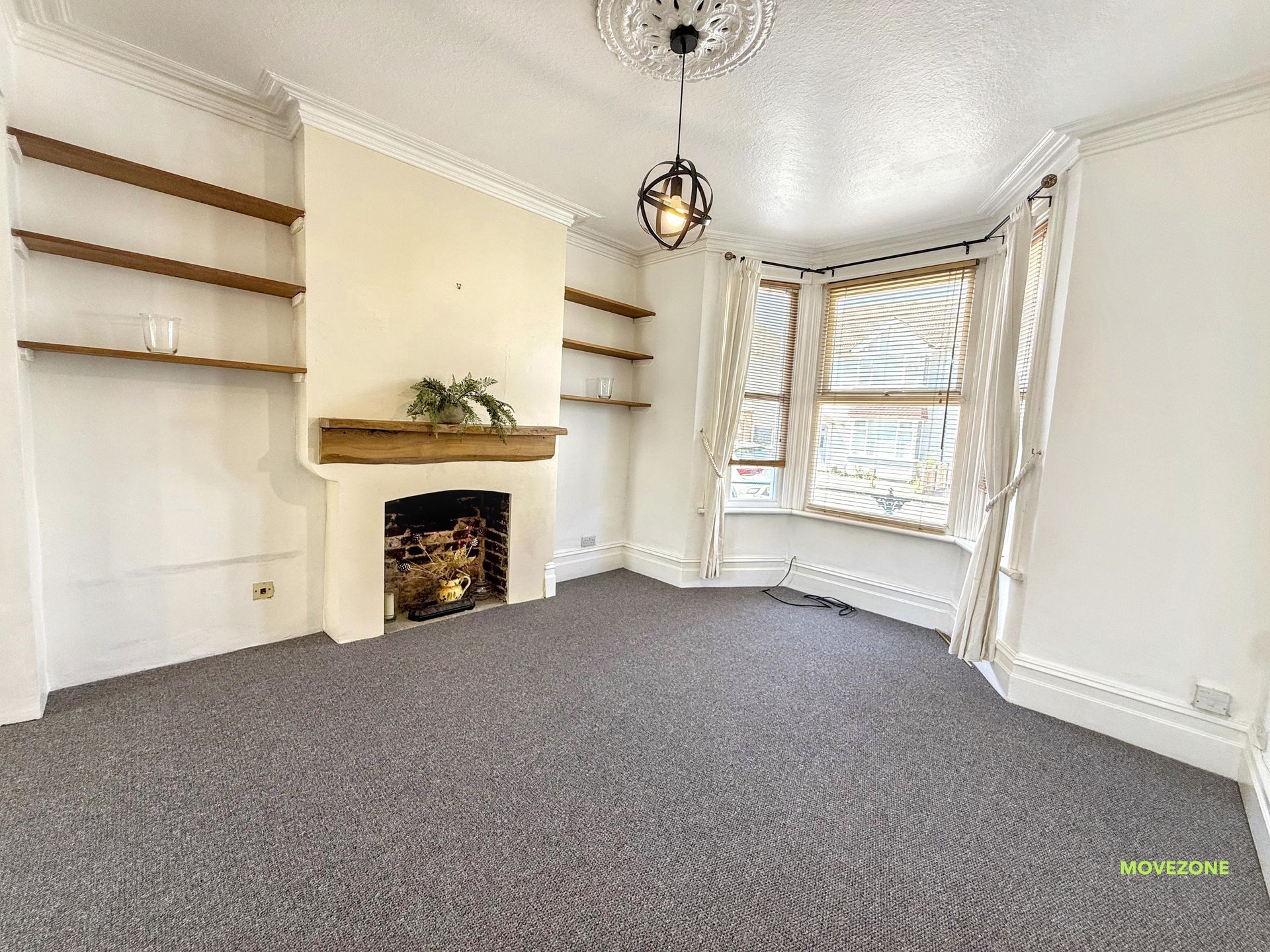 Bright empty living room with fireplace, bay window, built-in shelves, and gray carpet.