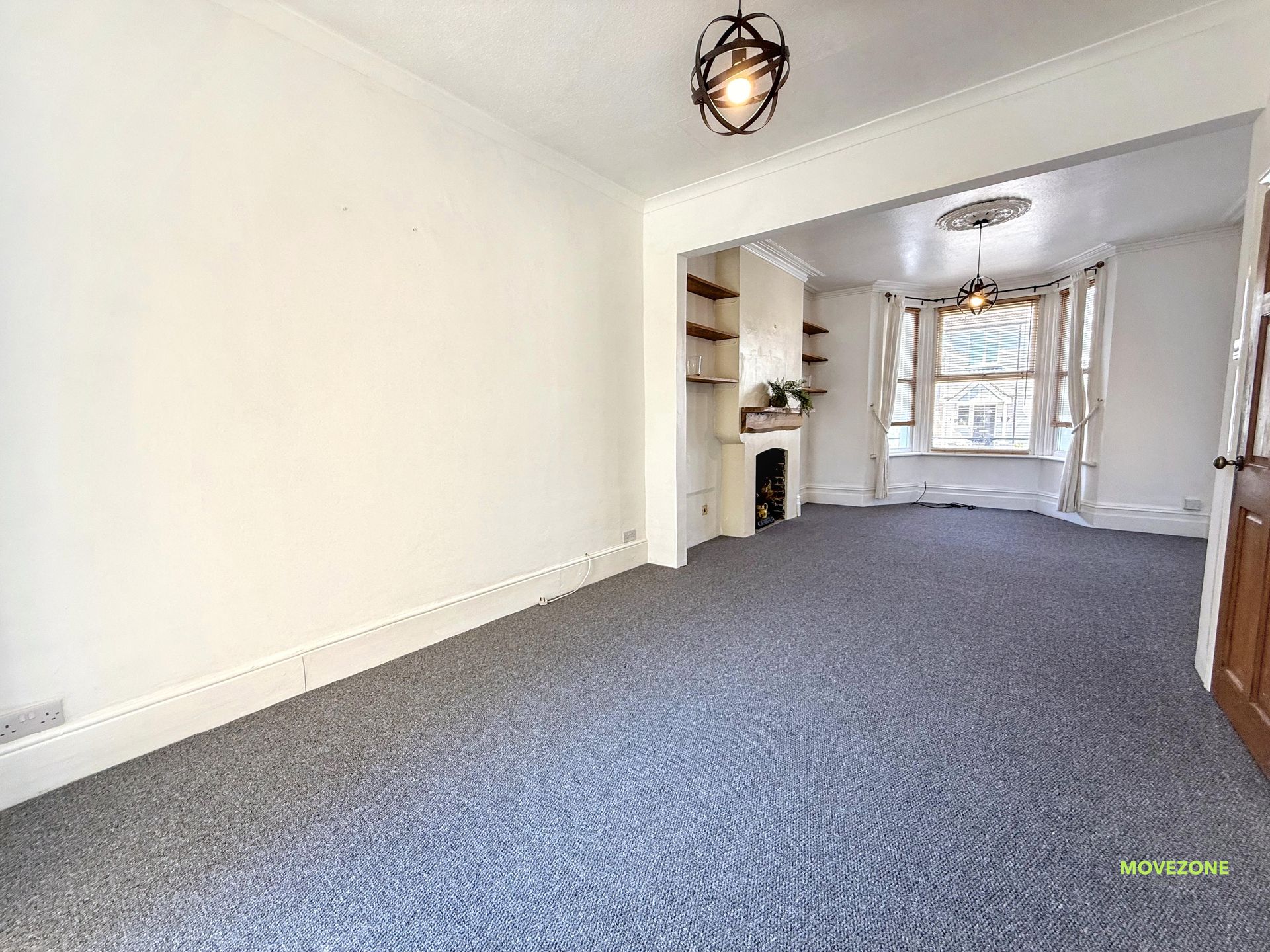 Empty carpeted living room with white walls, fireplace, bay window, and doorway to a second sitting area