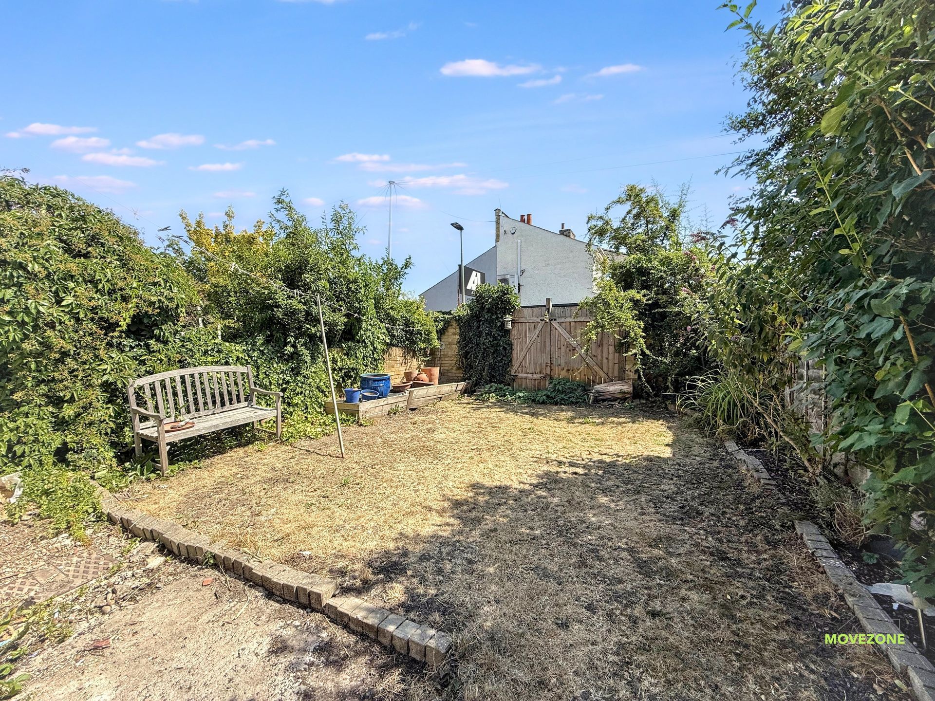 Sunny backyard with dry grass, a wooden bench, and dense hedges around a small garden path