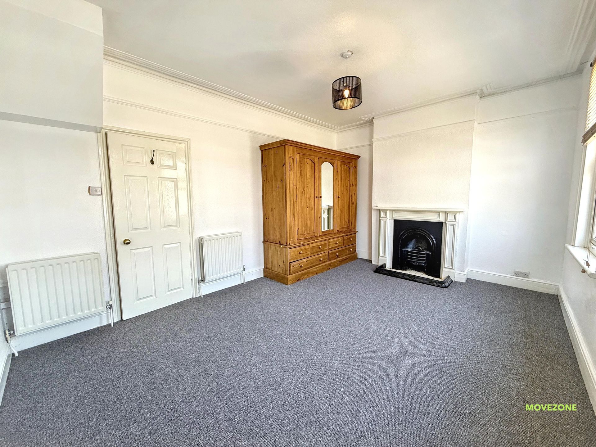 Empty white living room with gray carpet, fireplace, radiator, and wooden wardrobe
