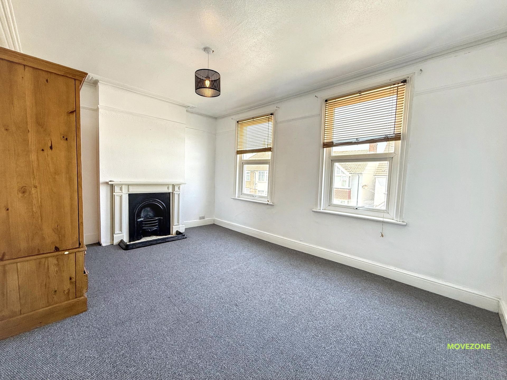 Empty carpeted living room with fireplace, wood wardrobe, and two windows with blinds
