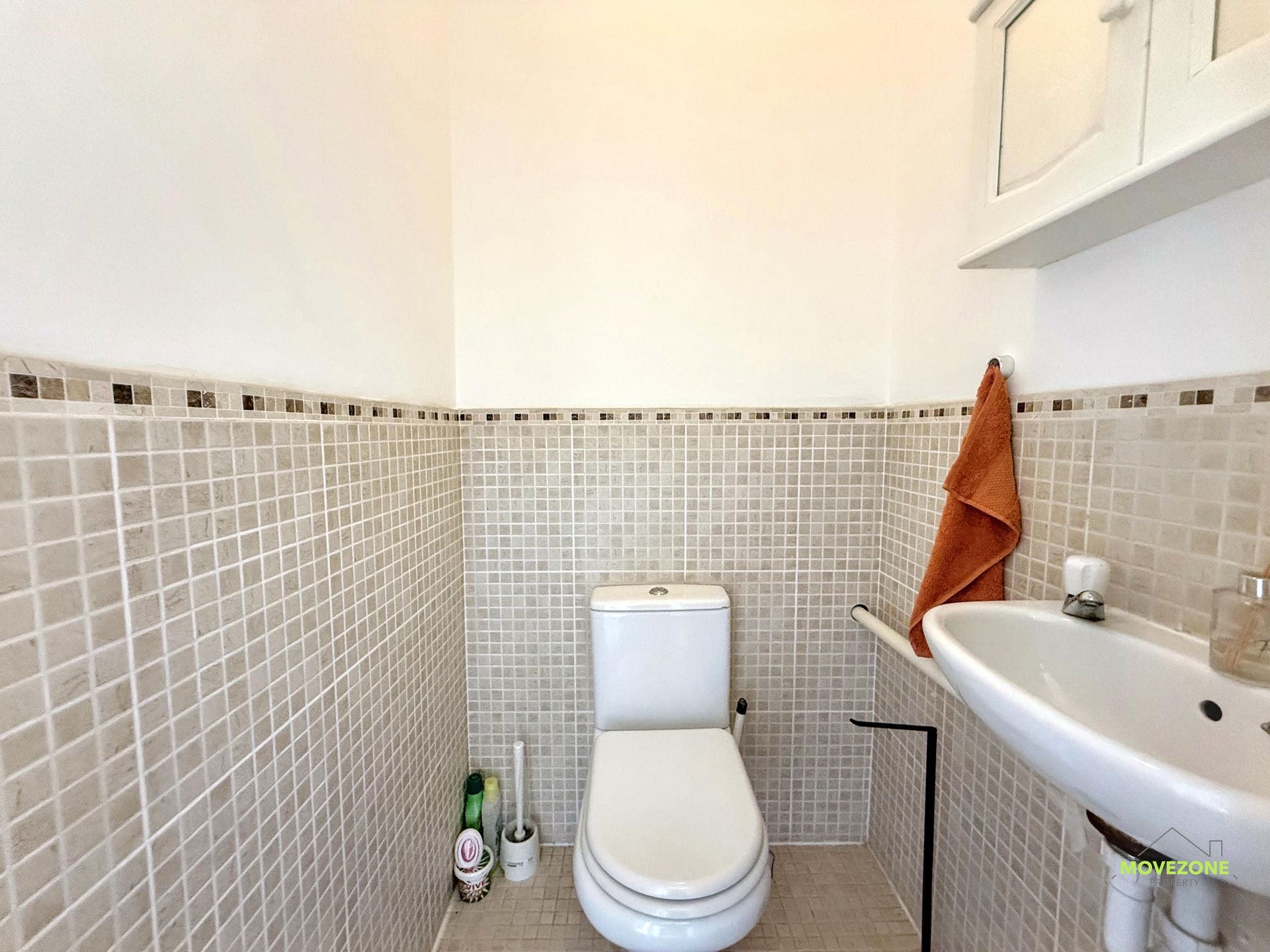 Small bathroom with a toilet, sink, tiled walls, and an orange towel hanging nearby.