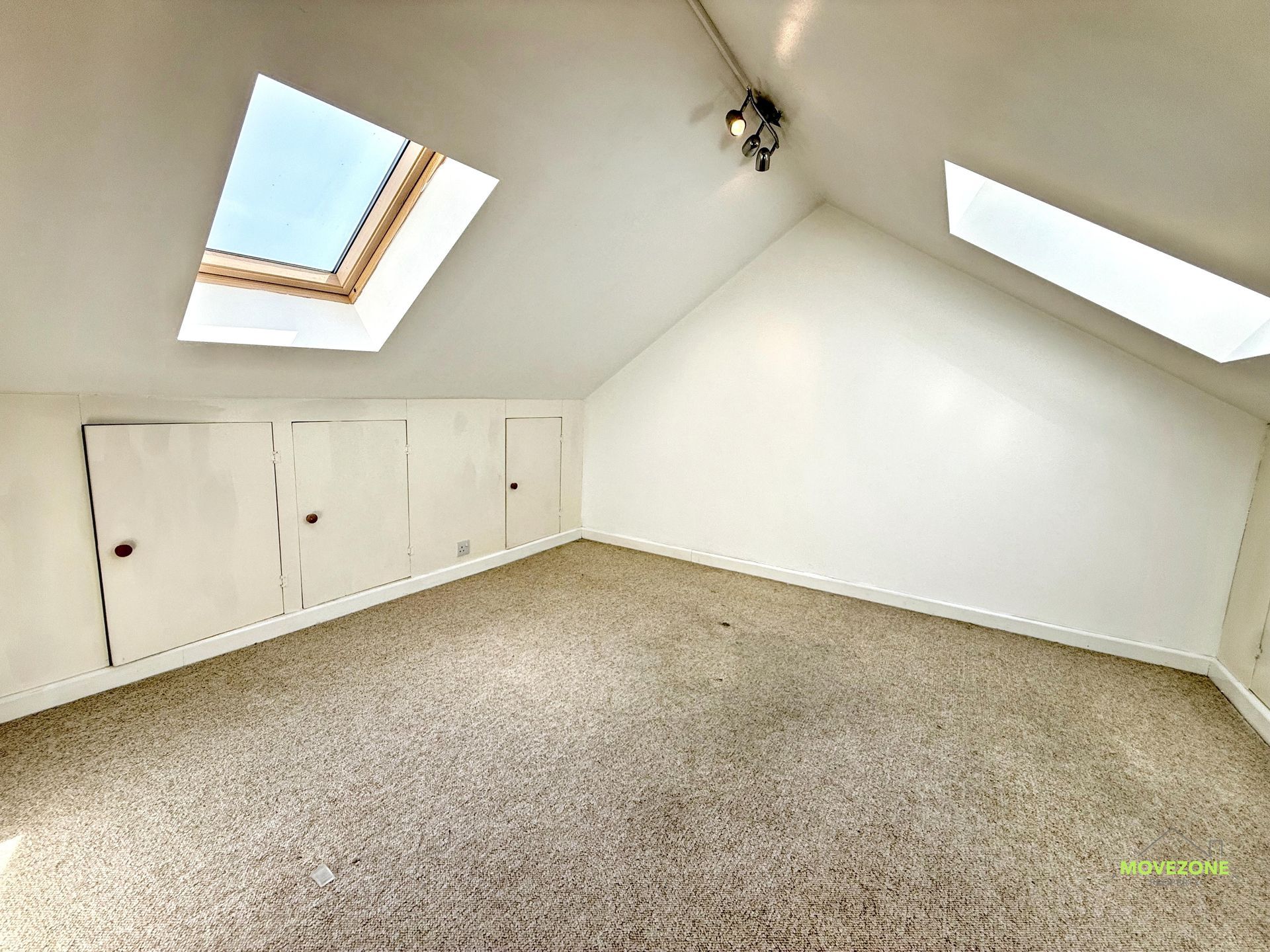 Empty carpeted attic room with sloped white ceiling, skylights, and built-in storage cabinets