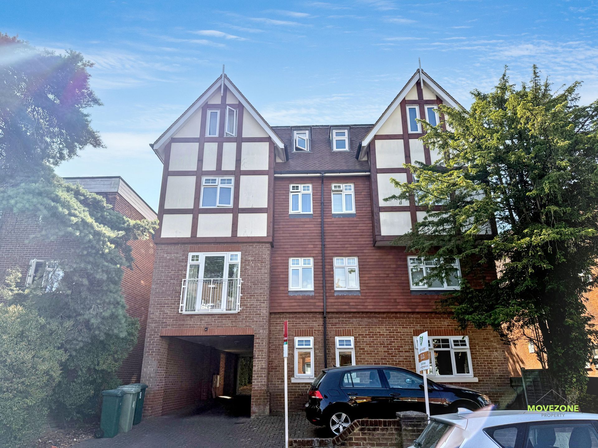 Brick apartment building with timber framing, parked car, and tree in front