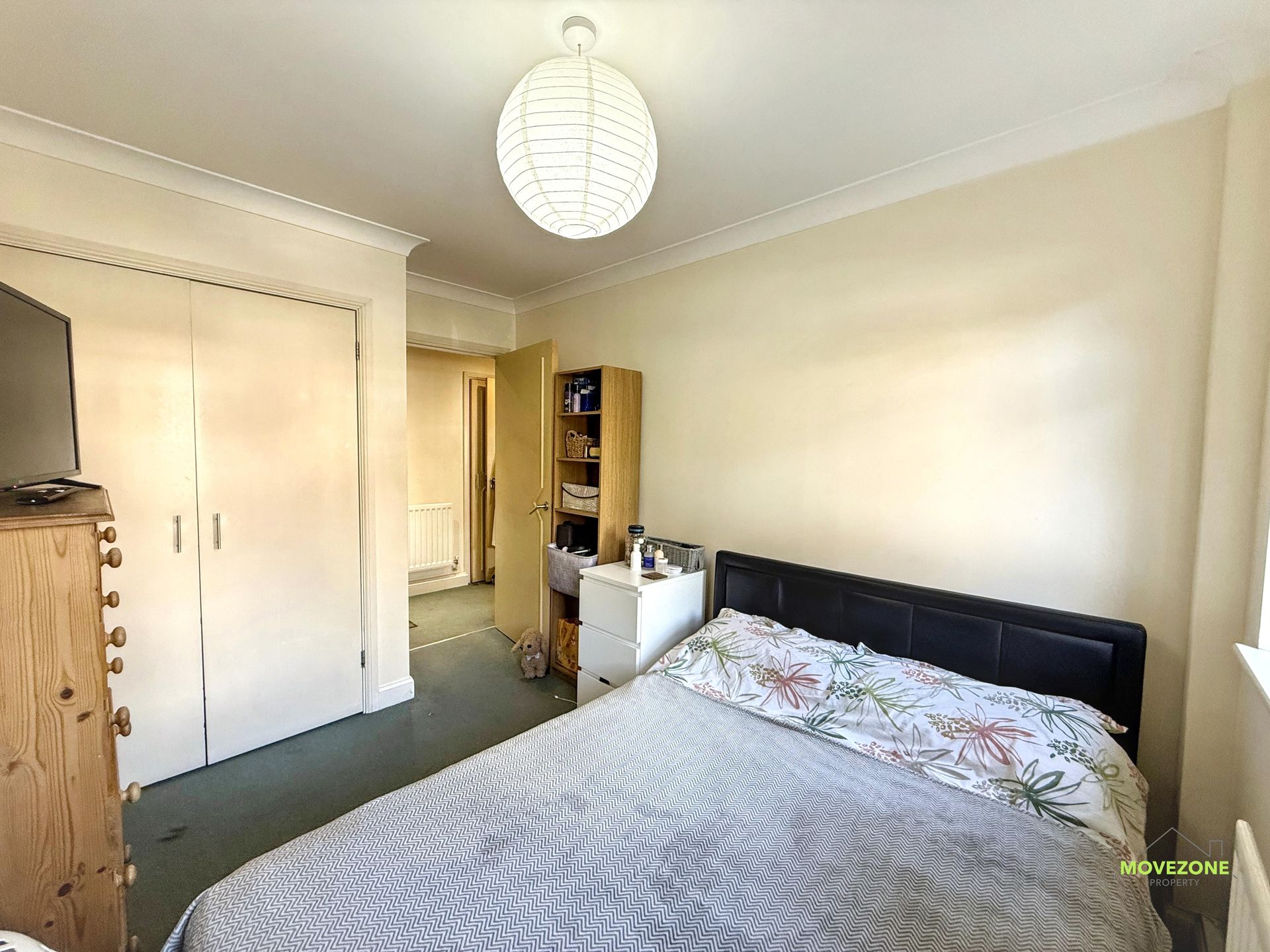 Bedroom with white wardrobe, bed, dresser, and open doorway in a beige room
