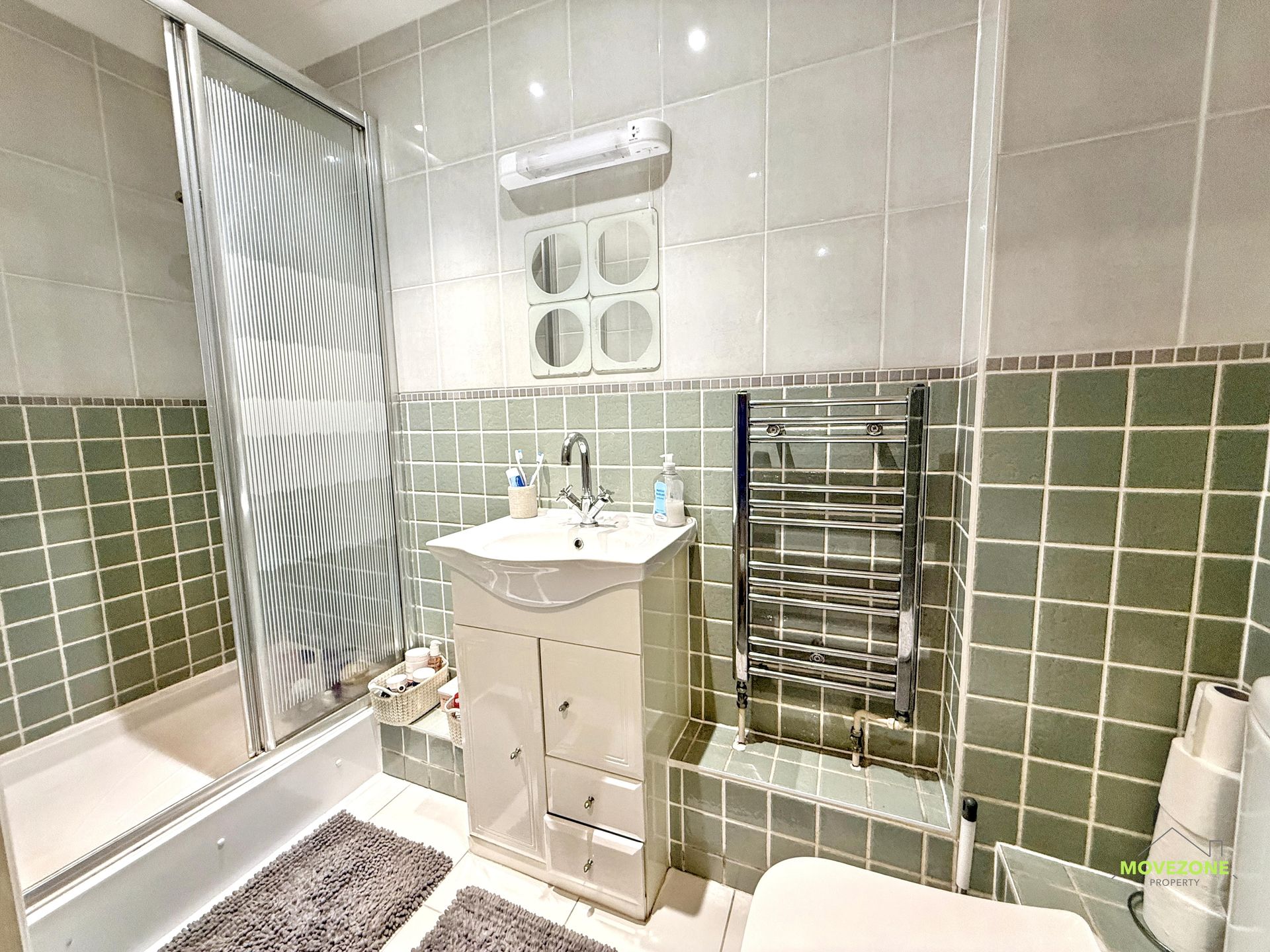 Small bathroom with a sink, bathtub, tiled walls, mirror cabinet, and towel radiator.