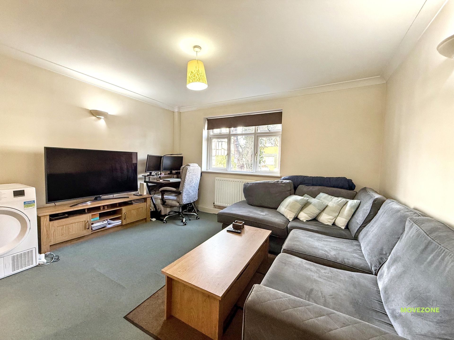 Bright living room with gray sectional sofa, TV, coffee table, and window with blinds