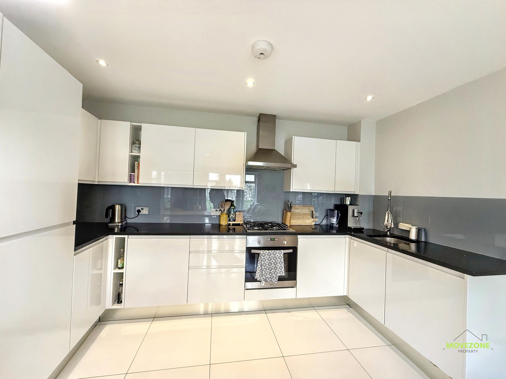 Modern white kitchen with black countertops, stainless steel appliances, and tiled floor