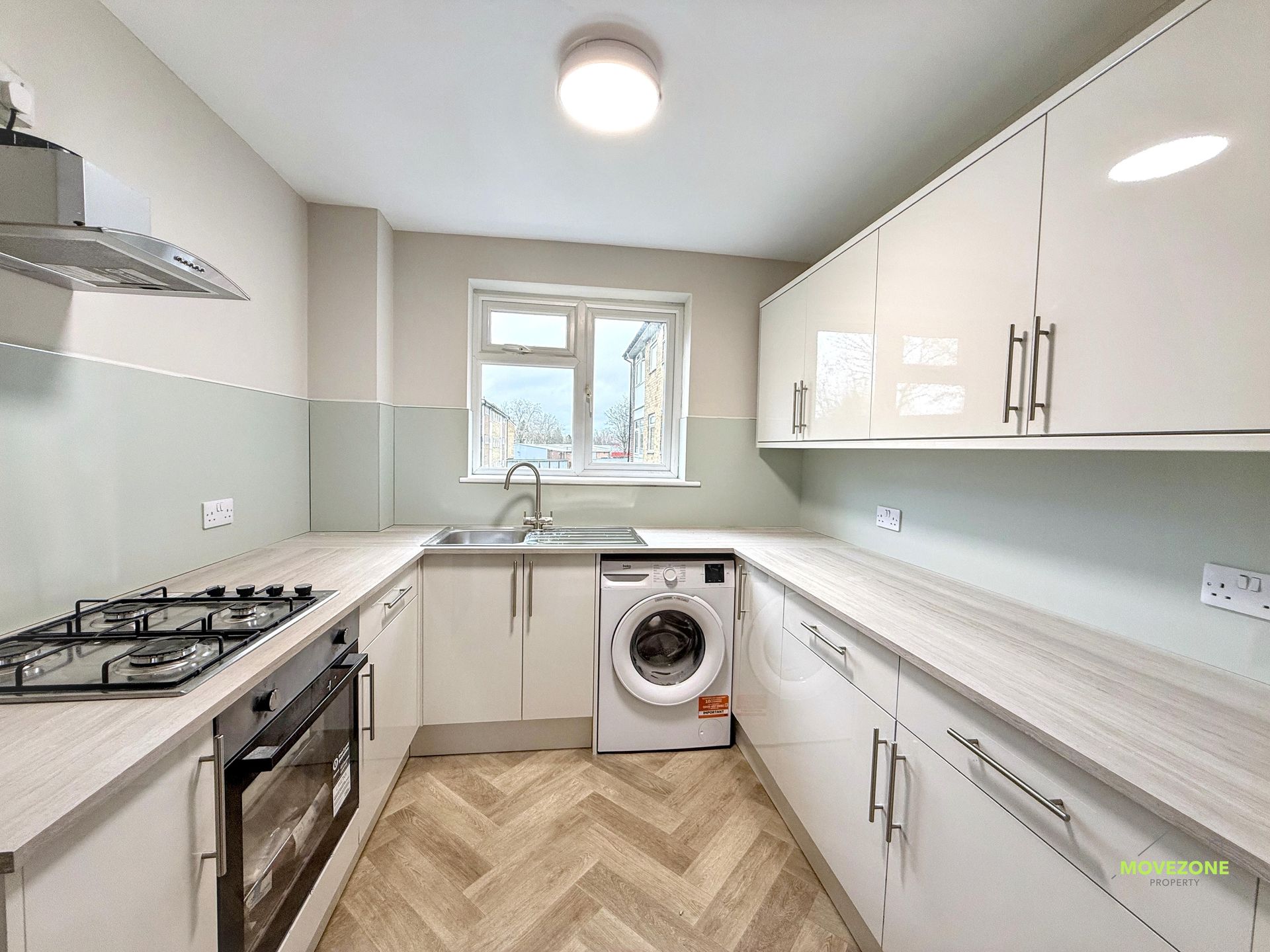 Bright modern kitchen with white cabinets, gas stove, washing machine, and window over the sink.