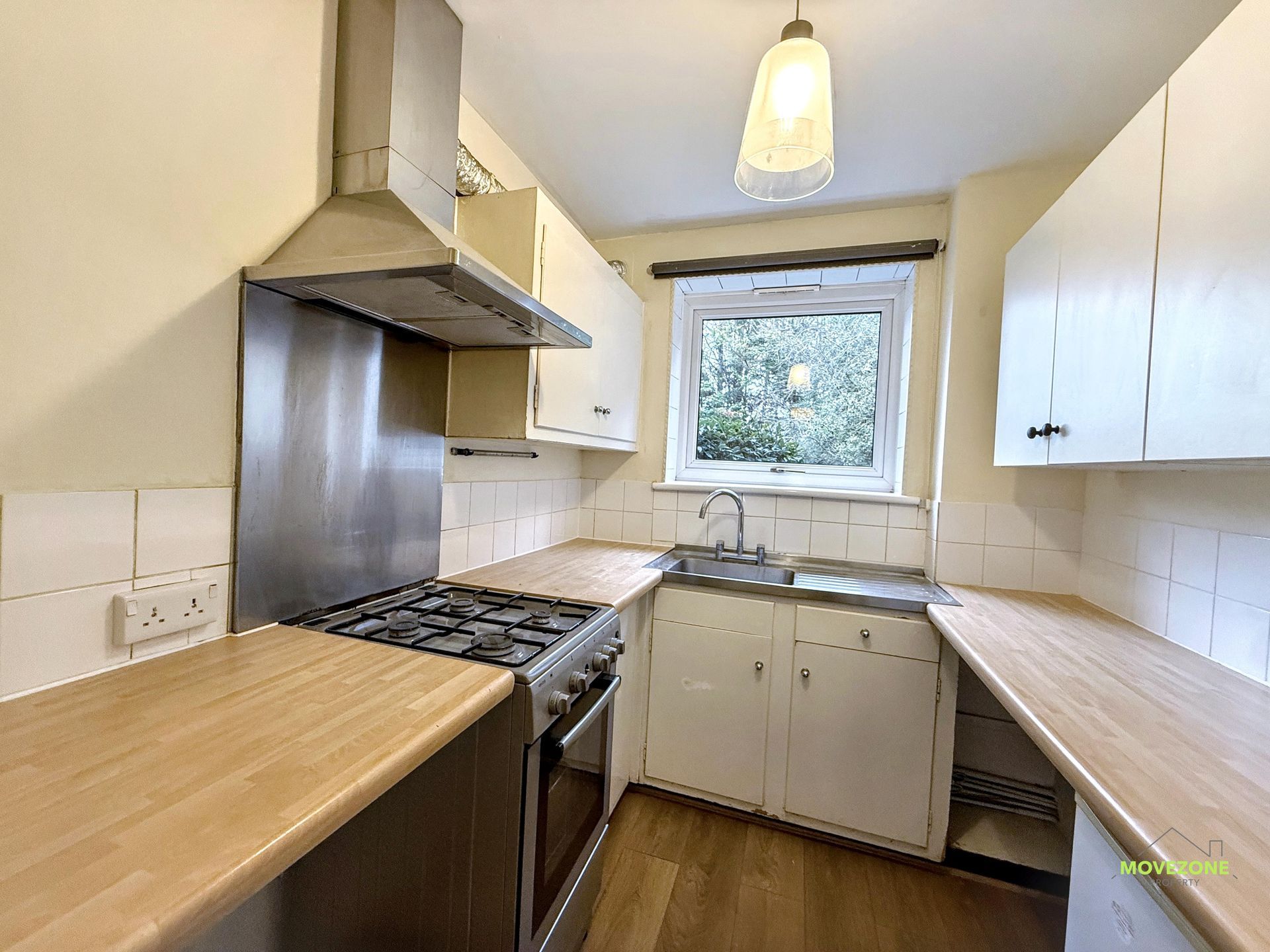 Compact galley kitchen with wood countertops, gas stove, white cabinets, and a window over the sink.