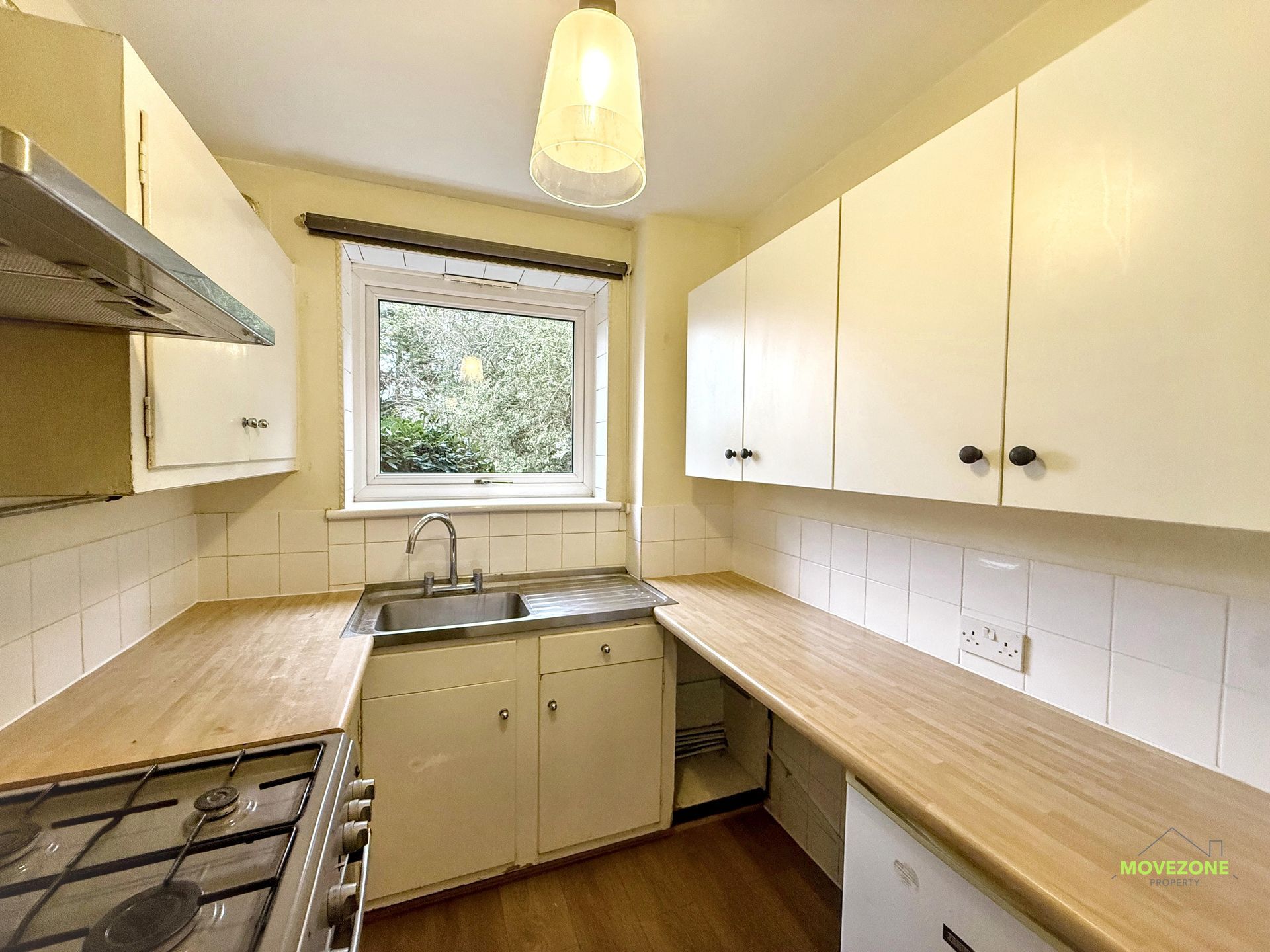 Narrow galley kitchen with white cabinets, wood countertops, sink under a window, and a gas stove.
