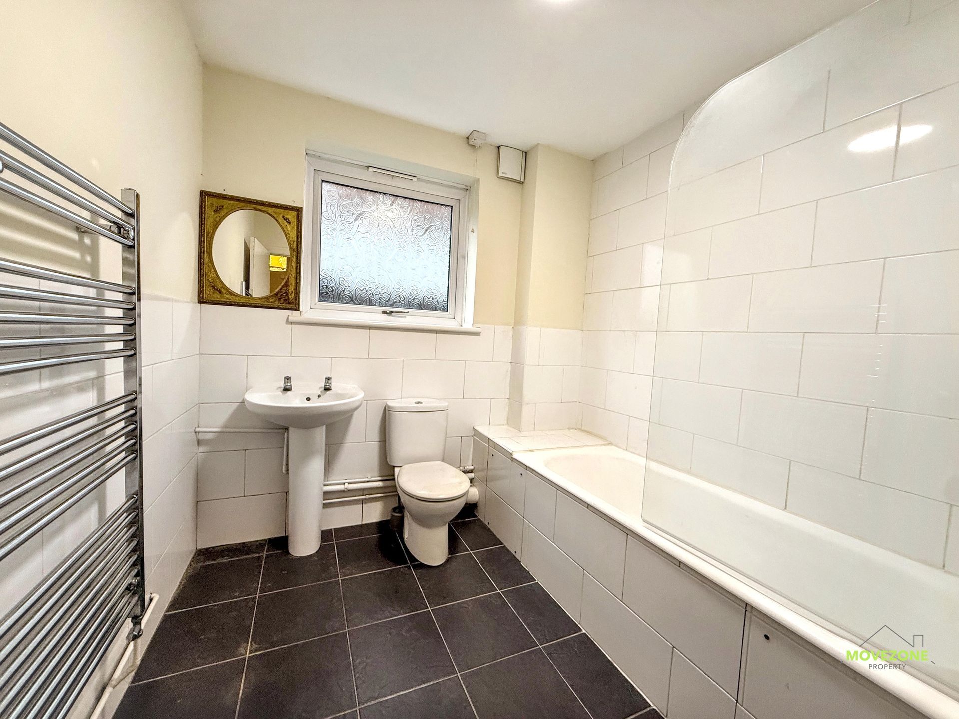 Small white bathroom with sink, toilet, bathtub, dark tile floor, and chrome towel radiator