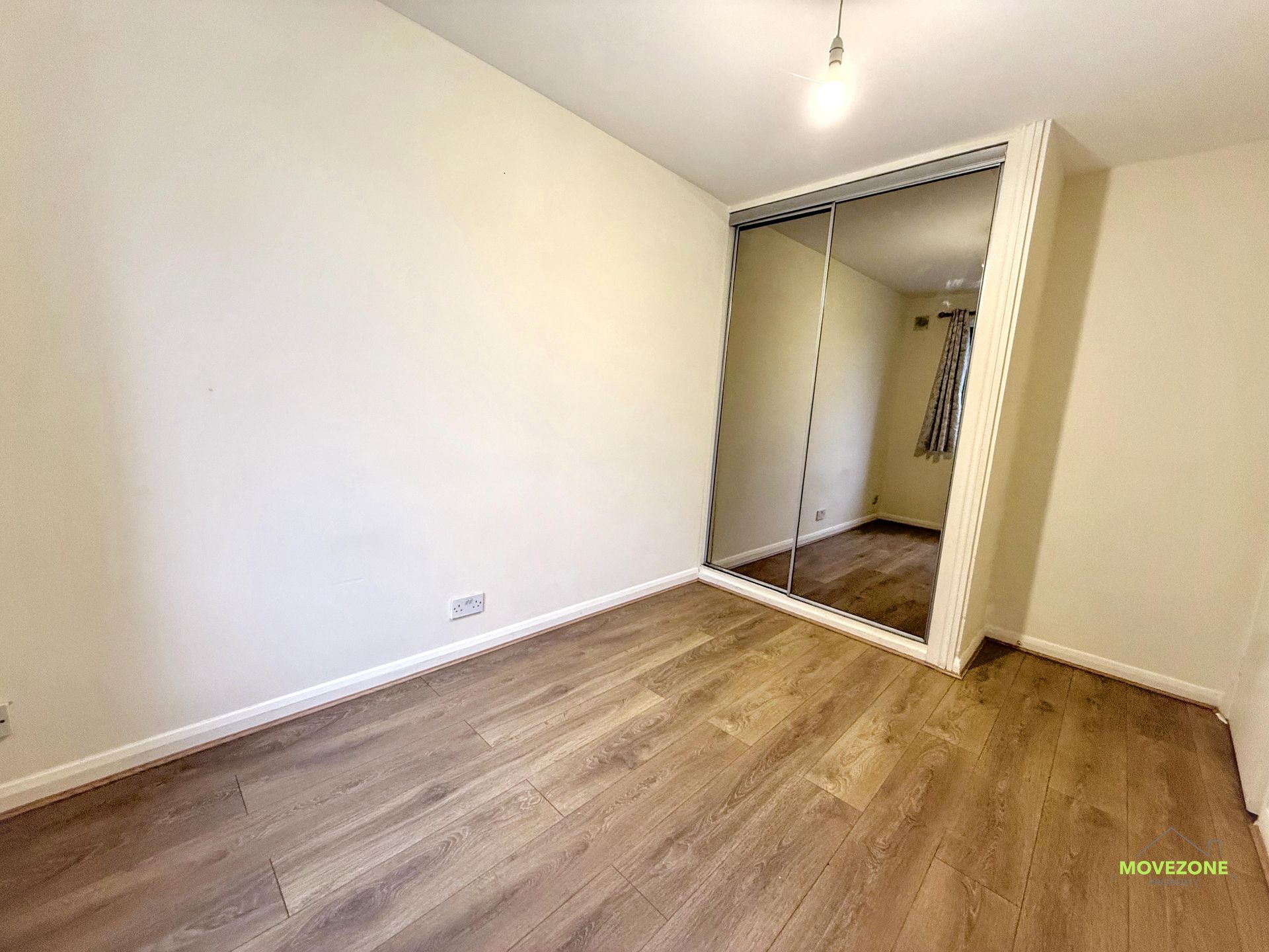 Empty beige bedroom with wood flooring and an open closet door.