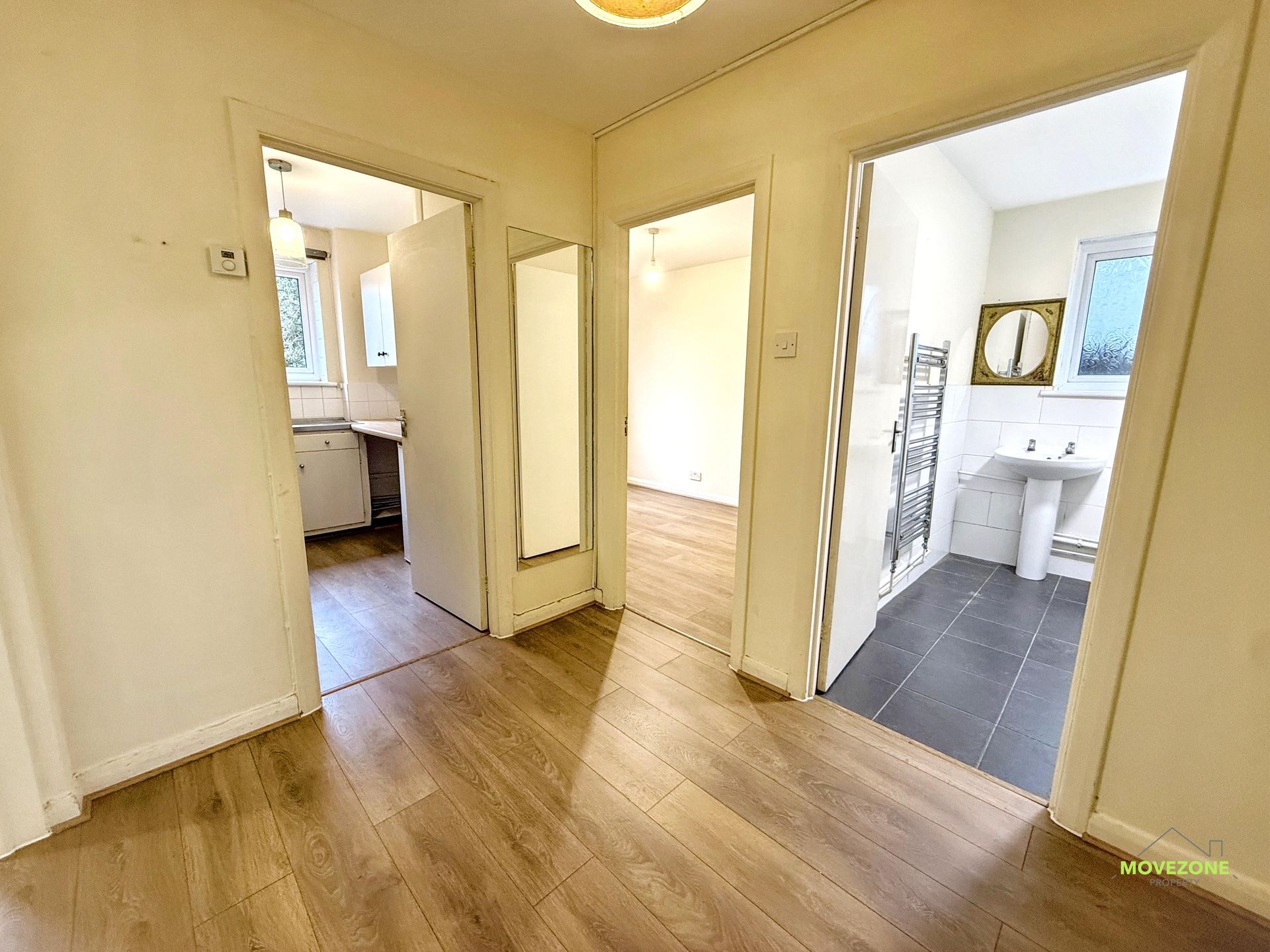 Bright hallway with wood floors, open doorways, and a tiled bathroom visible on the right.