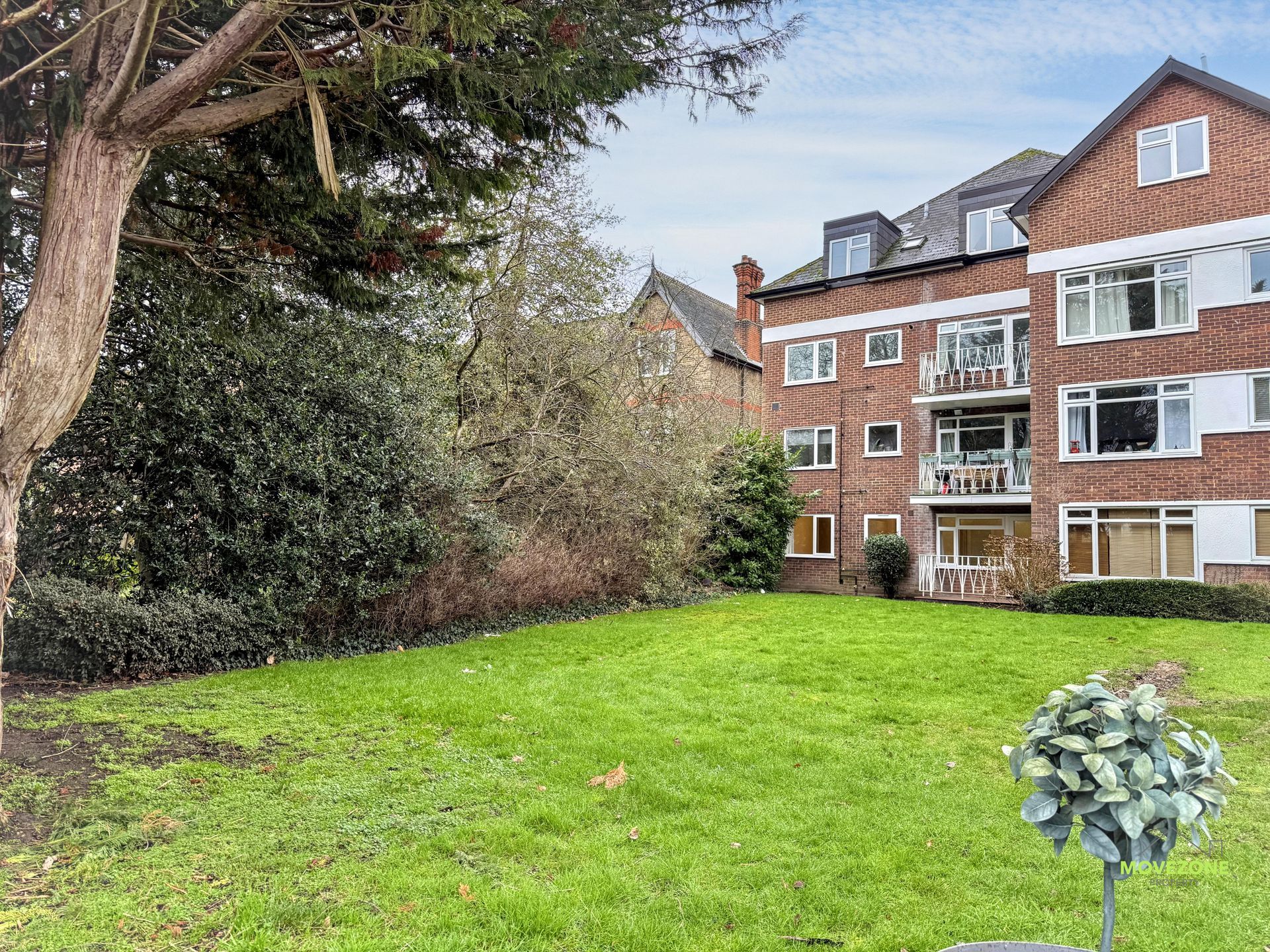 Grassy courtyard beside a brick apartment building with trees and shrubs